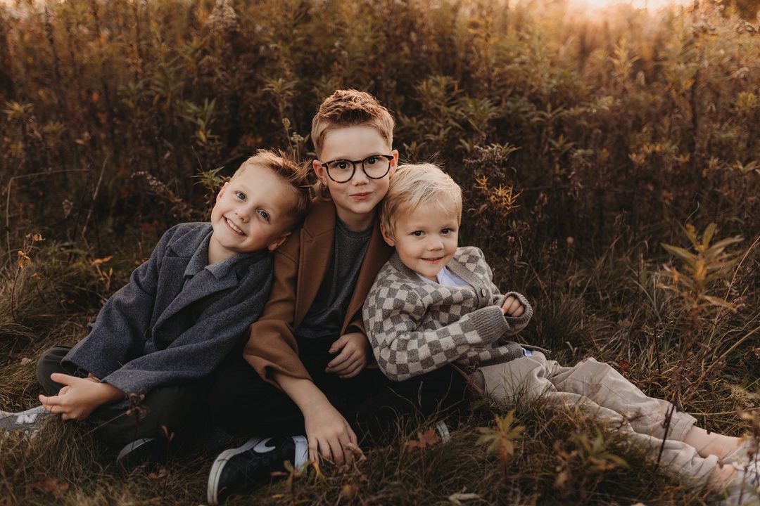 Three siblings smiling and hugging each other while sitting in a golden autumn field.