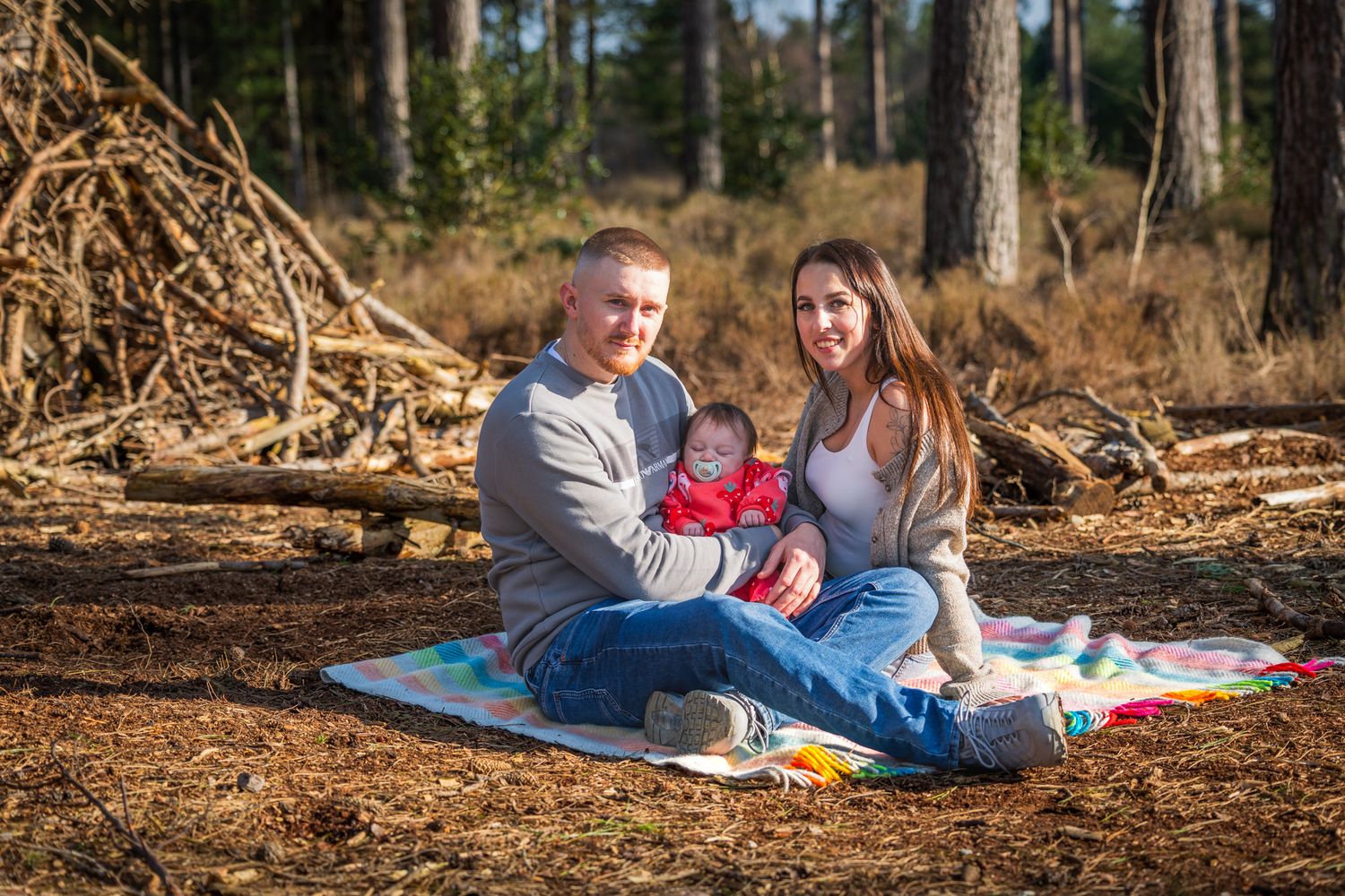 Young family with baby sitting on colorful blanket in sunny Dorset forest for outdoor picnic photo.