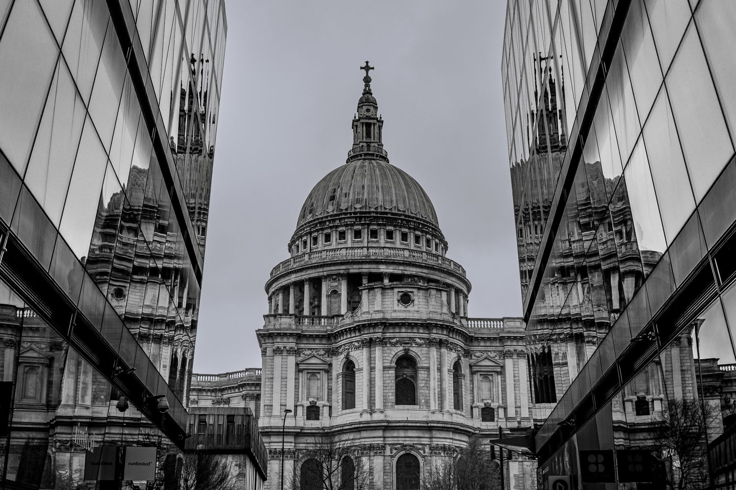 Black and white photo of St. Paul's Cathedral in London framed by modern glass buildings reflecting its iconic dome.