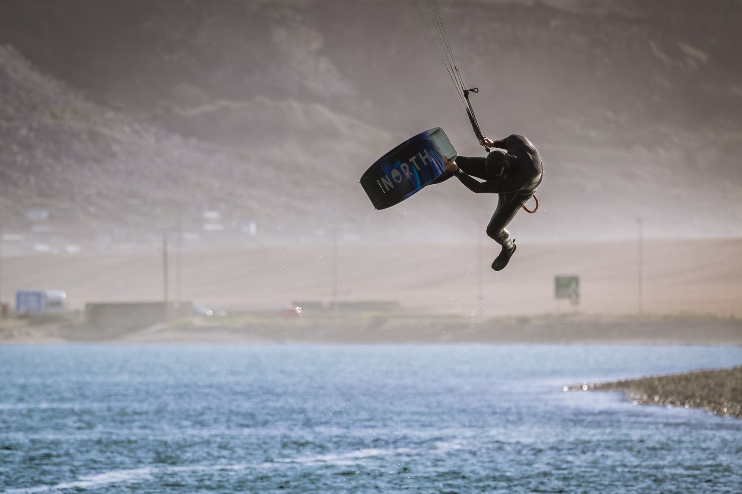 Kitesurfer performing aerial trick over choppy water with Isle of Portland backdrop on a windy day in Dorset.