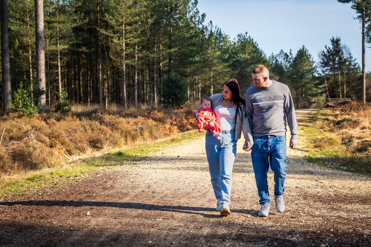 Couple walking together on a forest path surrounded by tall pine trees and autumn foliage on a sunny day in Dorset.