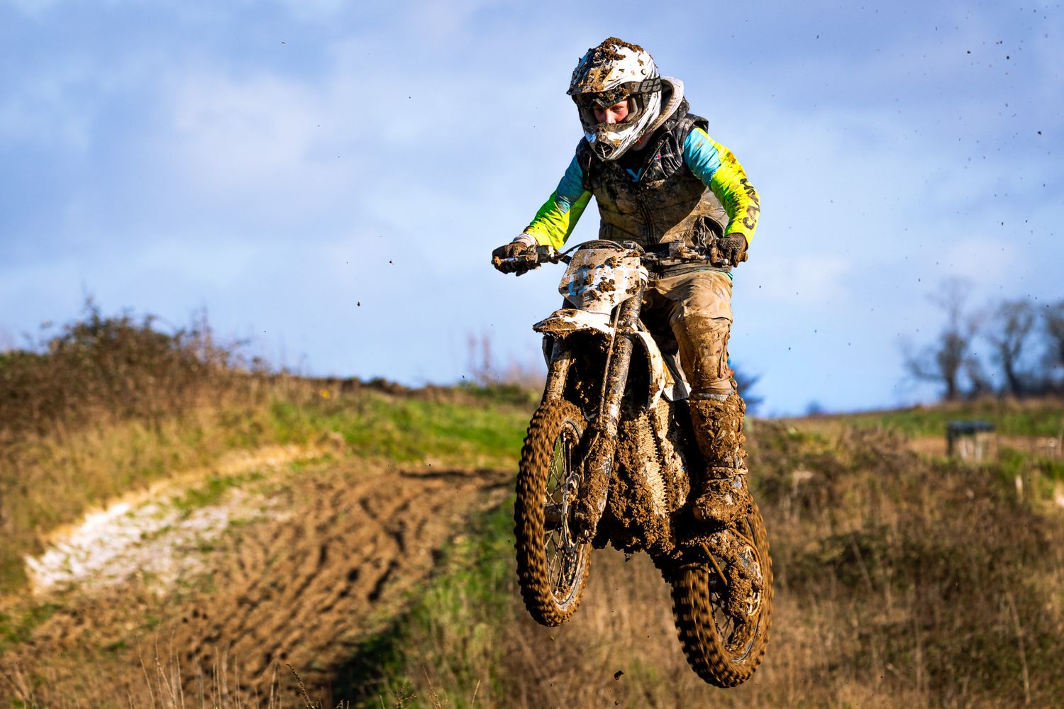Muddy motocross rider catches air on a dirt bike during an off-road race on a rugged outdoor track.
