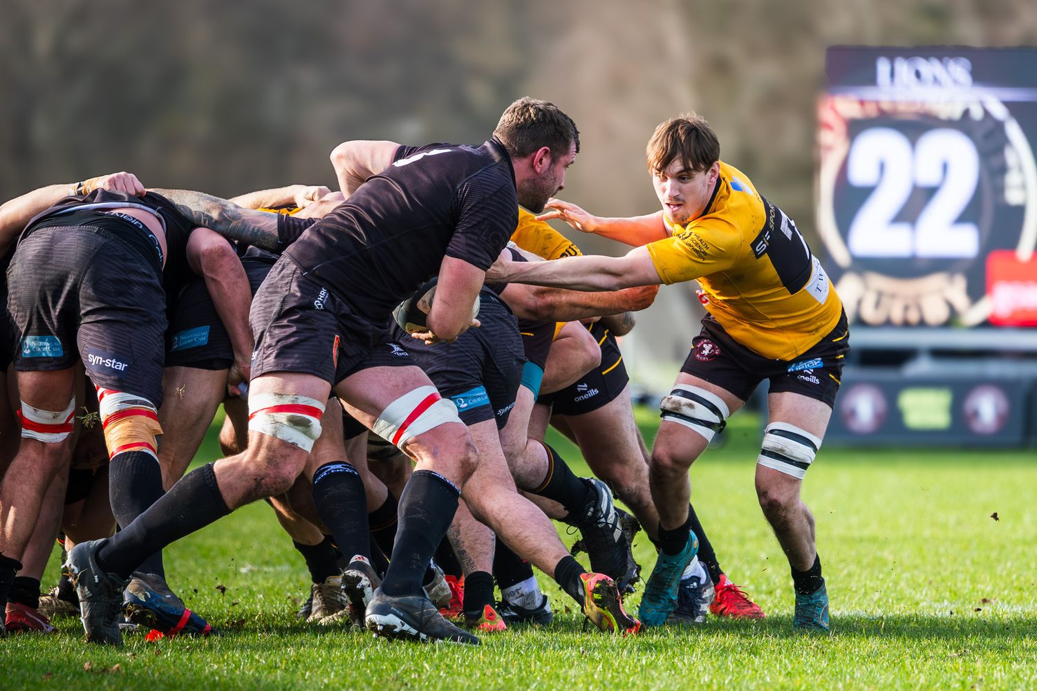 Rugby players compete in an intense scrum during a match, with players in black and yellow jerseys pushing against each other.