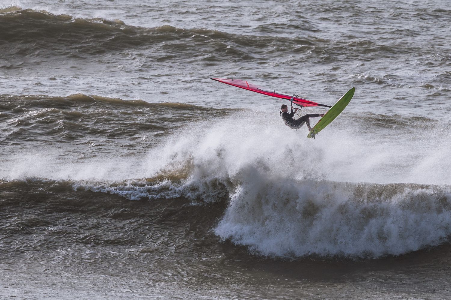Windsurfer riding a large wave with a red and green sail in rough ocean conditions at Kimmeridge in Dorset.