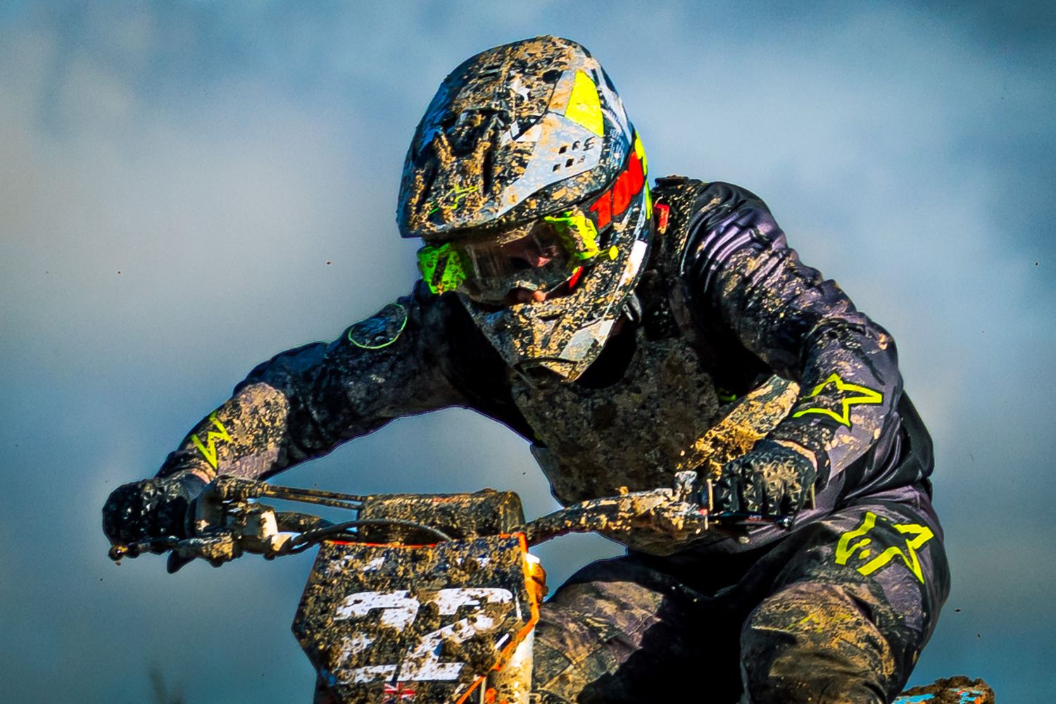 Muddy motocross rider wearing a helmet and goggles races bike number 22 through a dirt track.