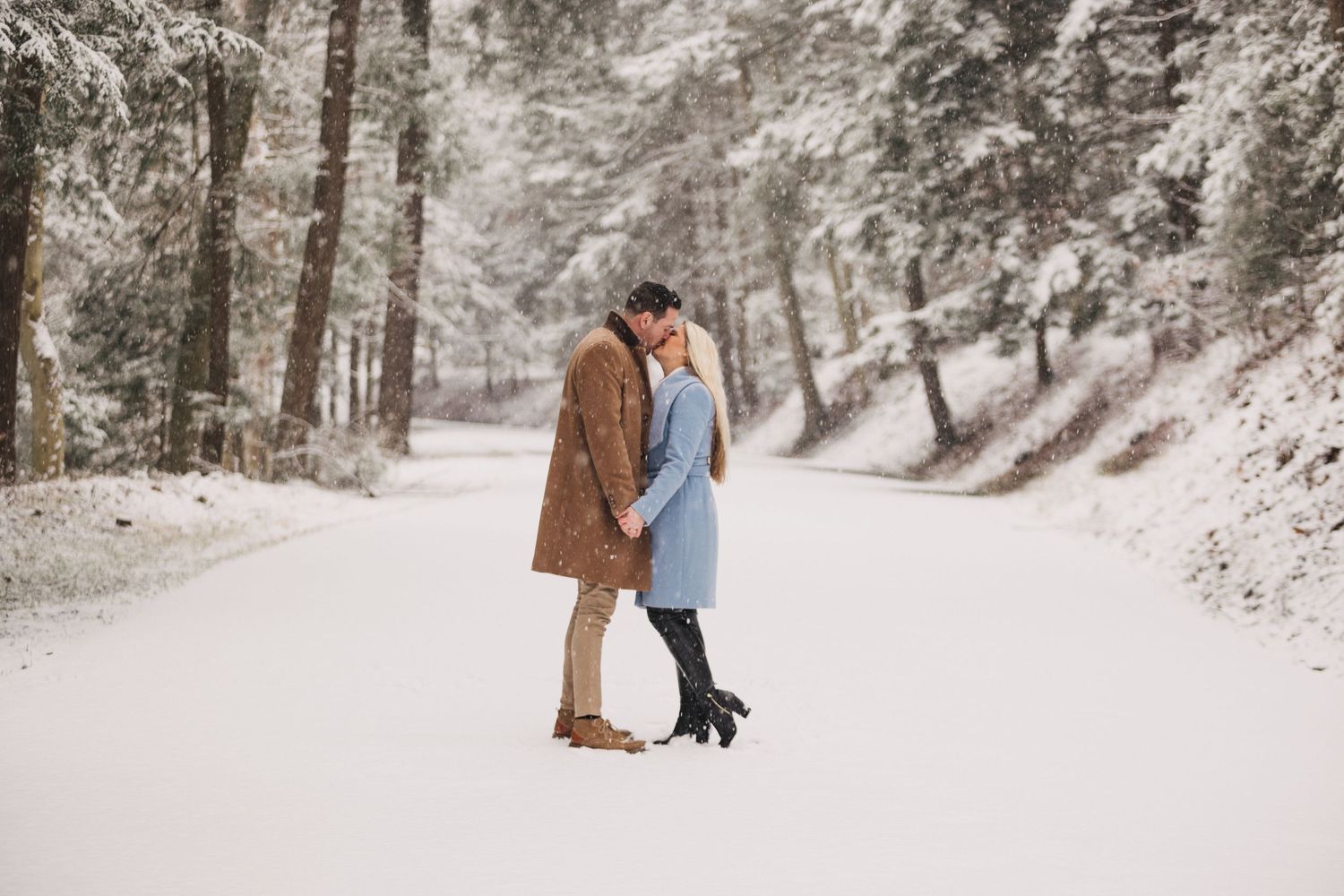 A romantic winter engagement photo series showing a couple walking through snow-covered woods.
