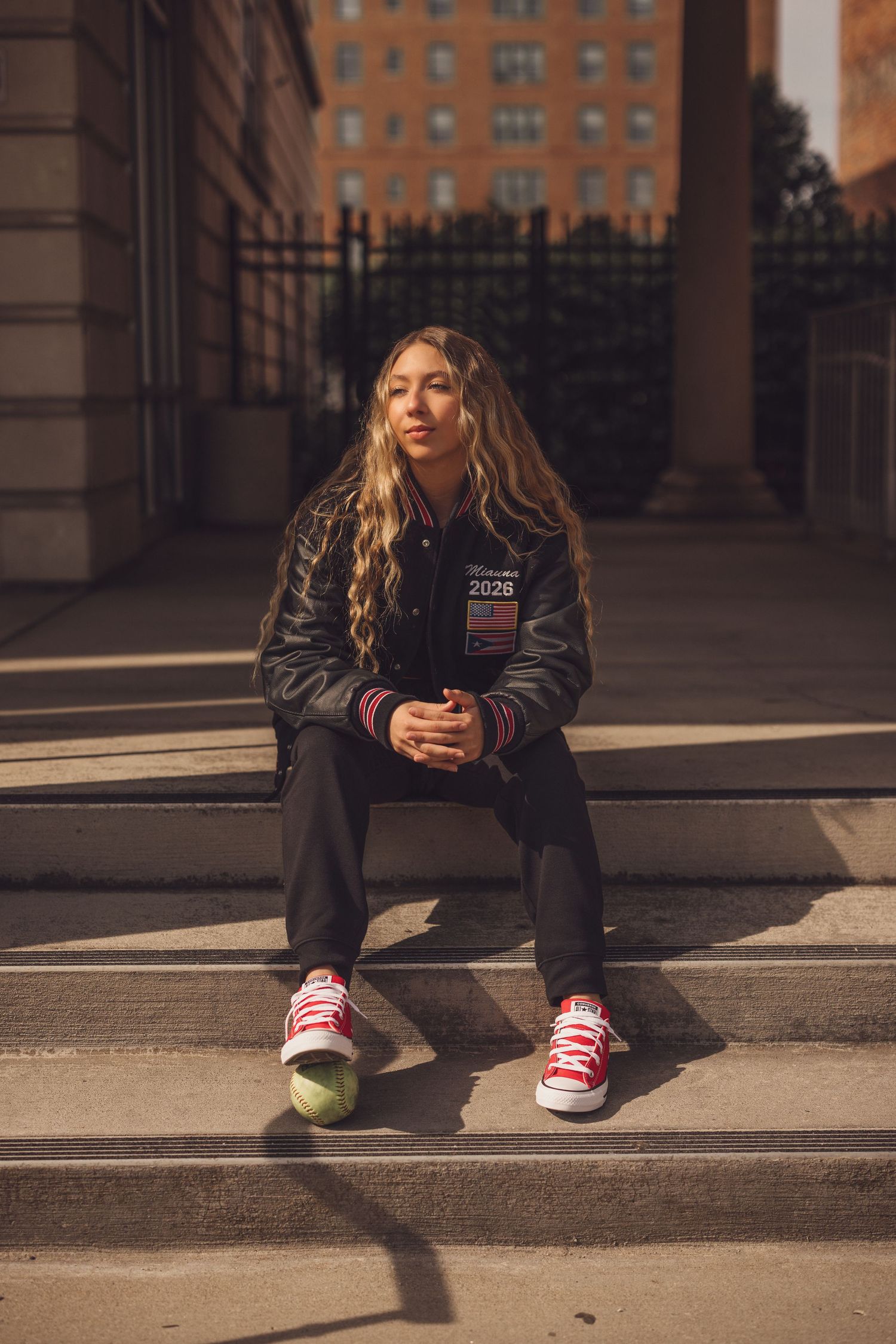 Person in dark jacket and sneakers sits on concrete steps in urban setting.