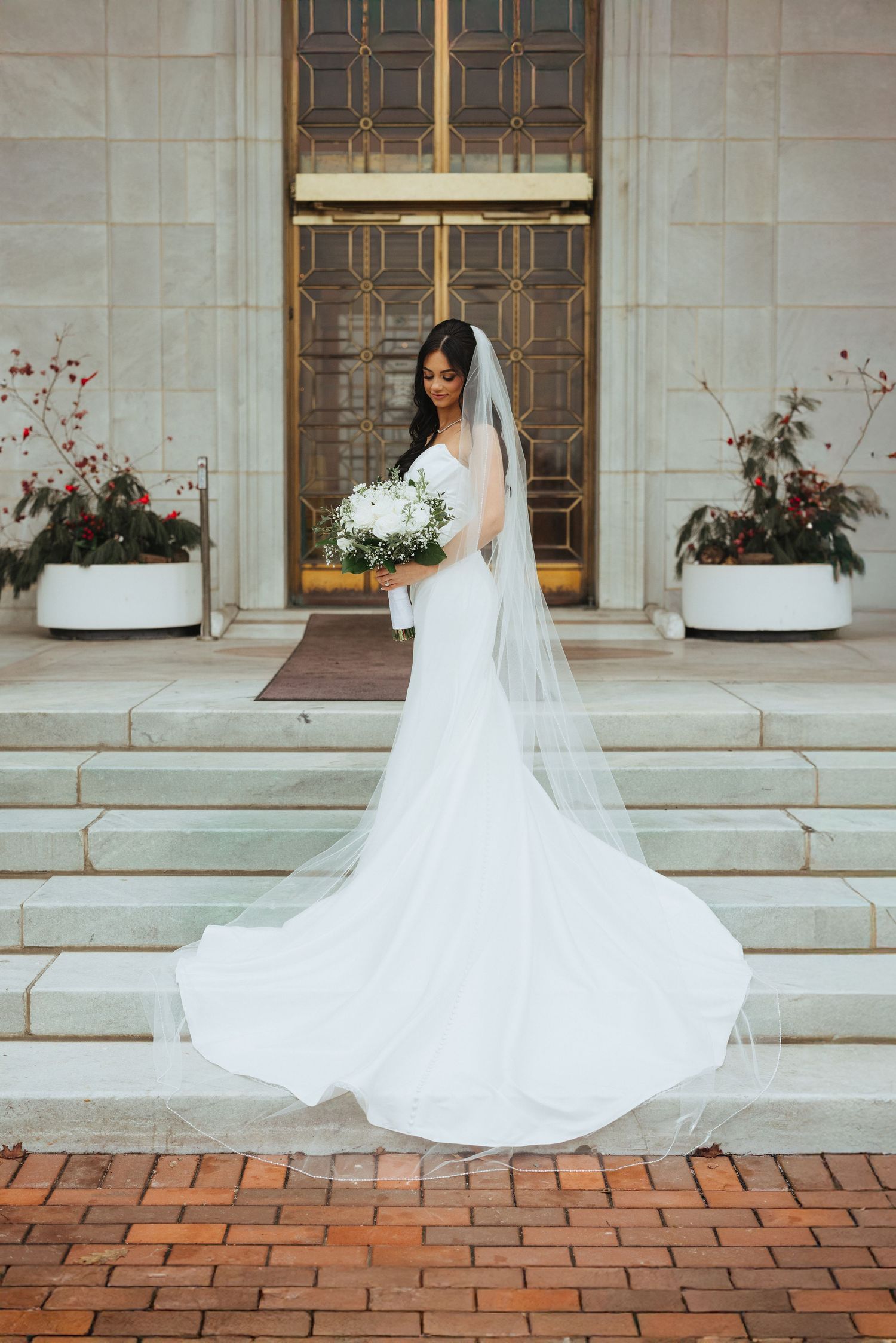 Bride in flowing white gown and veil poses on classic stone steps.