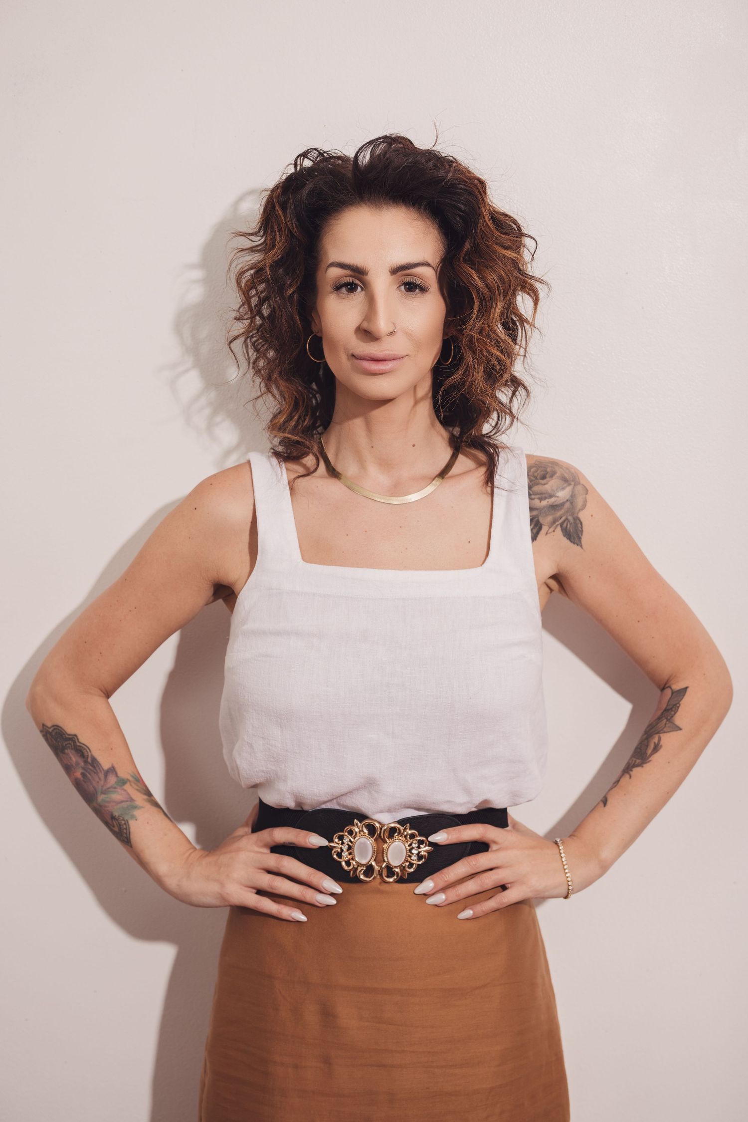 Fashion portrait in white tank top and brown skirt with decorative belt.