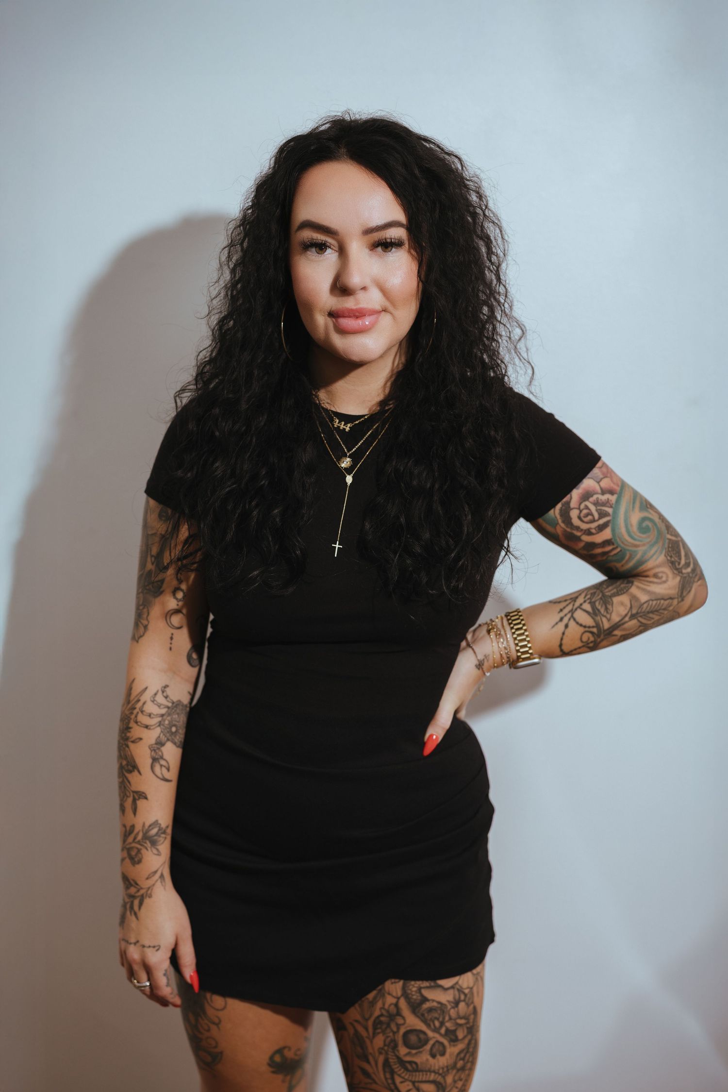 Portrait of tattooed person in black outfit against light studio background.