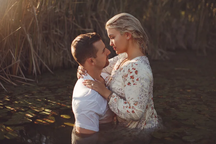 Intimate couples portrait session in dramatic lighting against dark natural background.