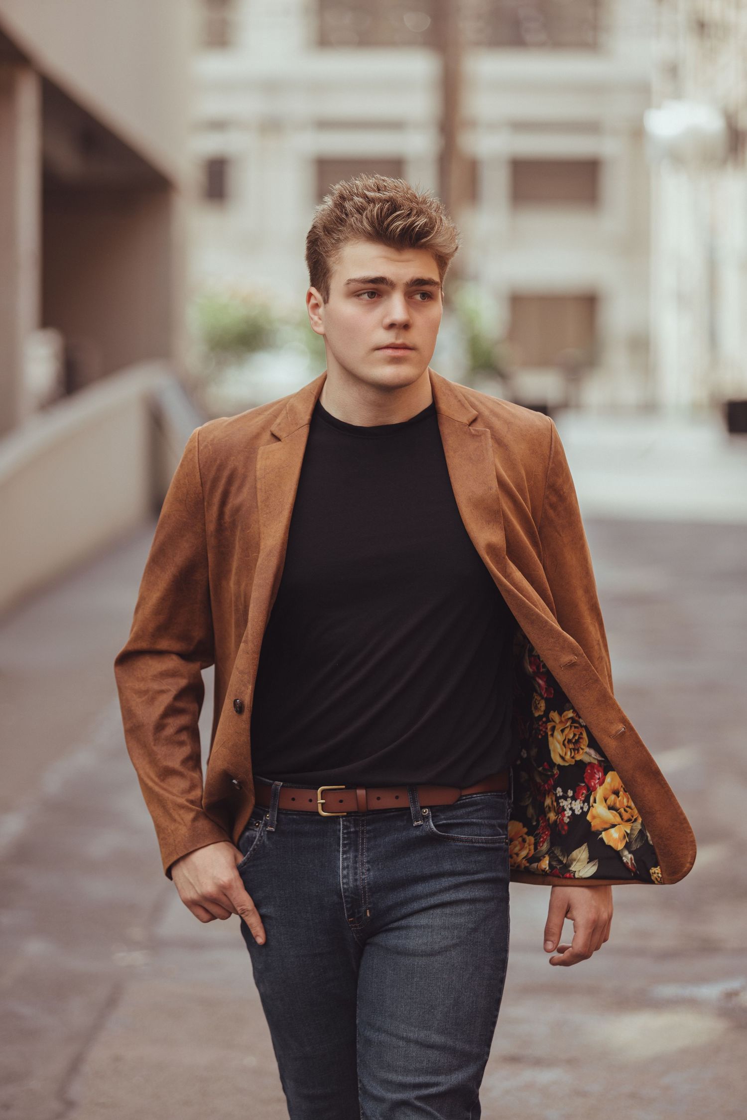 Person wearing brown blazer and black shirt walks confidently through urban setting.