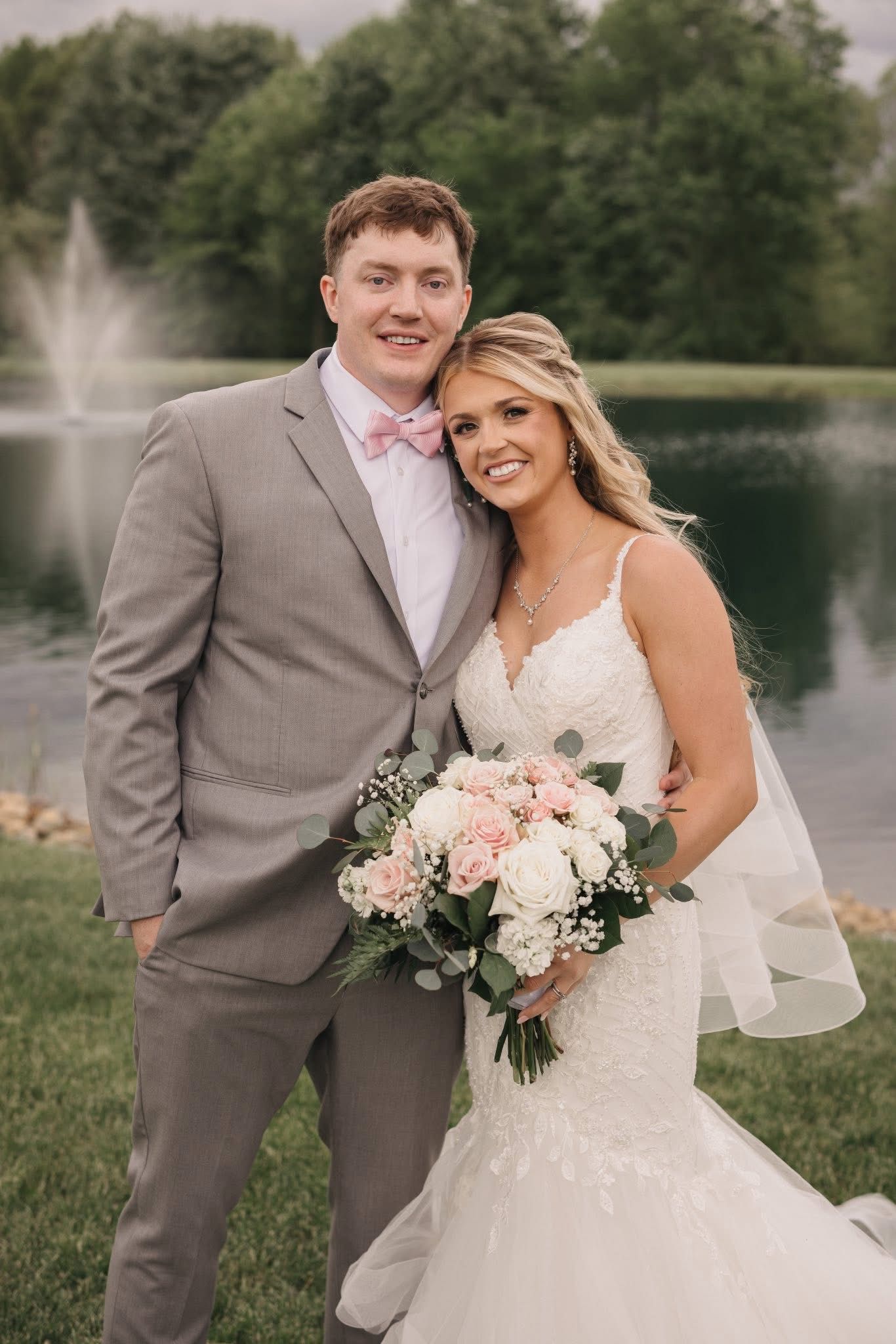 Joyful wedding portraits by lake with fountain in background.