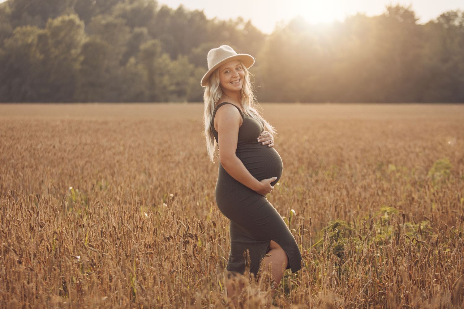 Golden hour maternity session in a wheat field with dramatic sunset lighting.