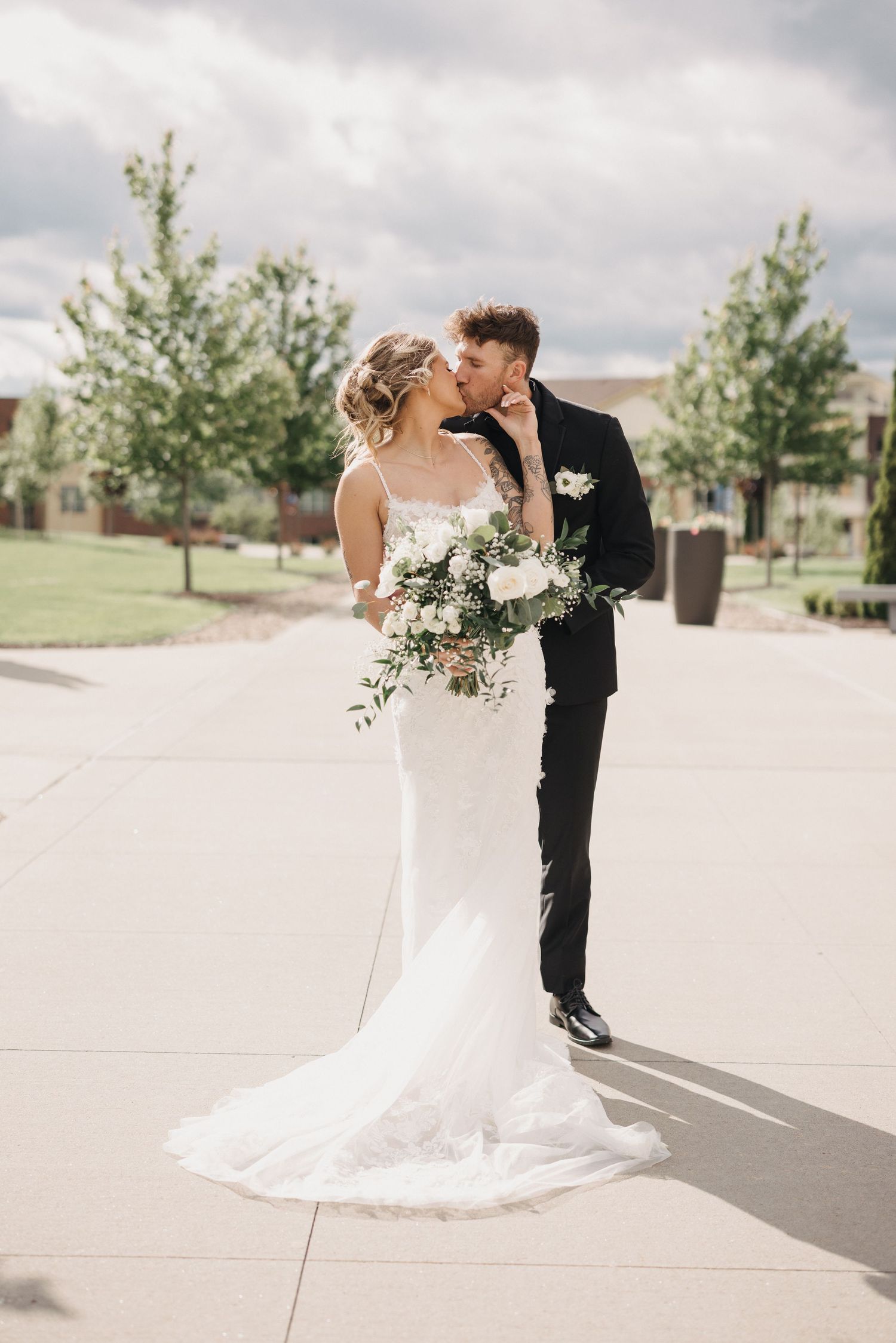 Wedding couple shares romantic moments on a bright concrete plaza with trees in background.
