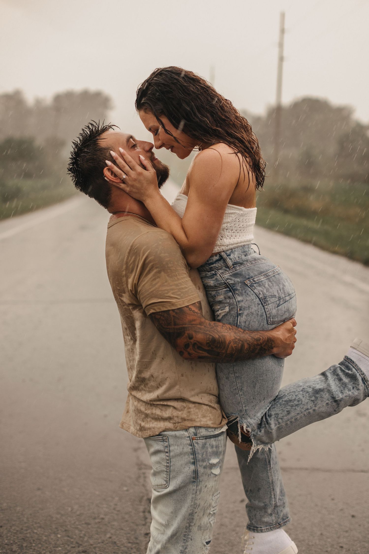 Couple embracing in the rain on empty road during moody photoshoot.