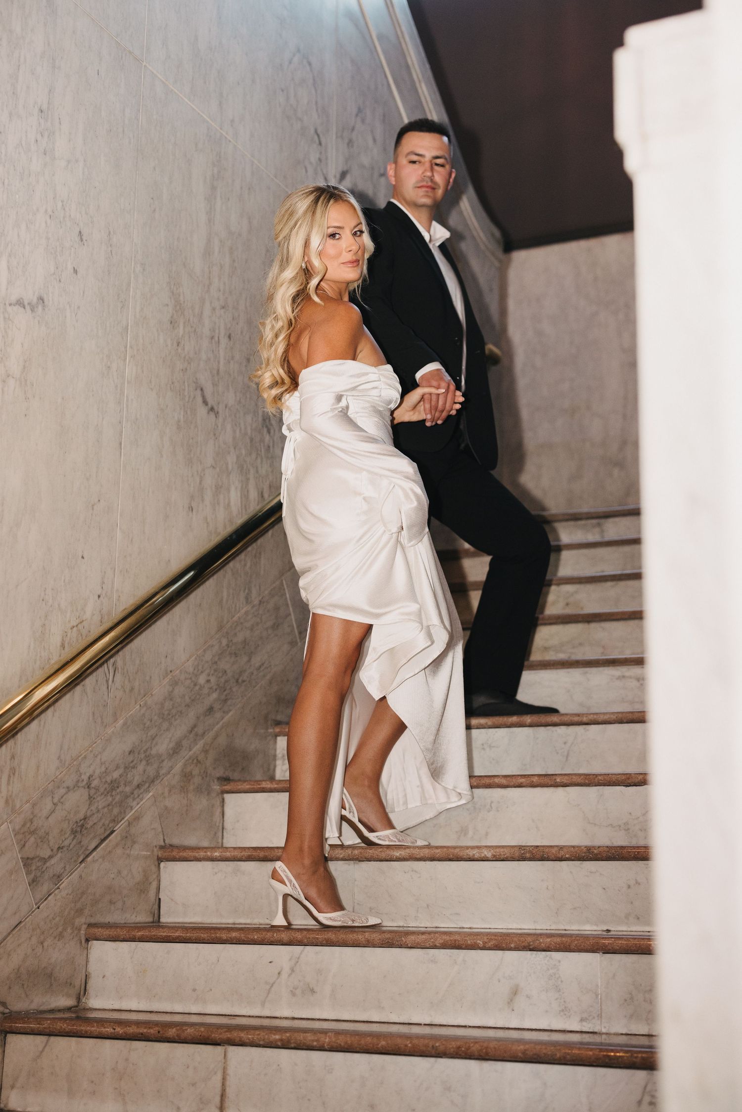 Couple walking up concrete stairs in formal attire during wedding photoshoot.