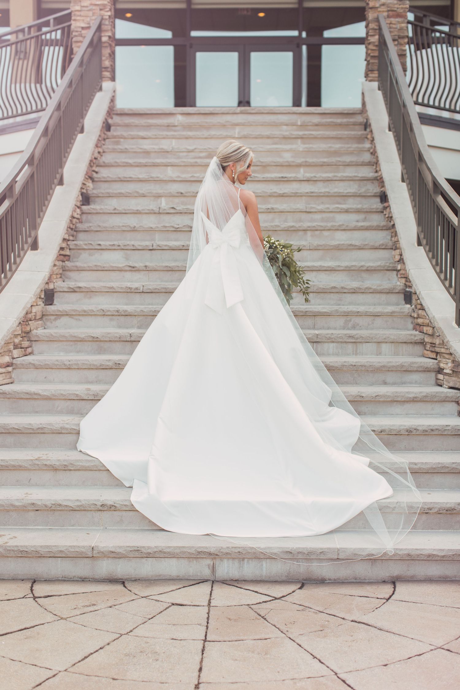 A flowing white wedding dress with a long train cascades down elegant stone steps.
