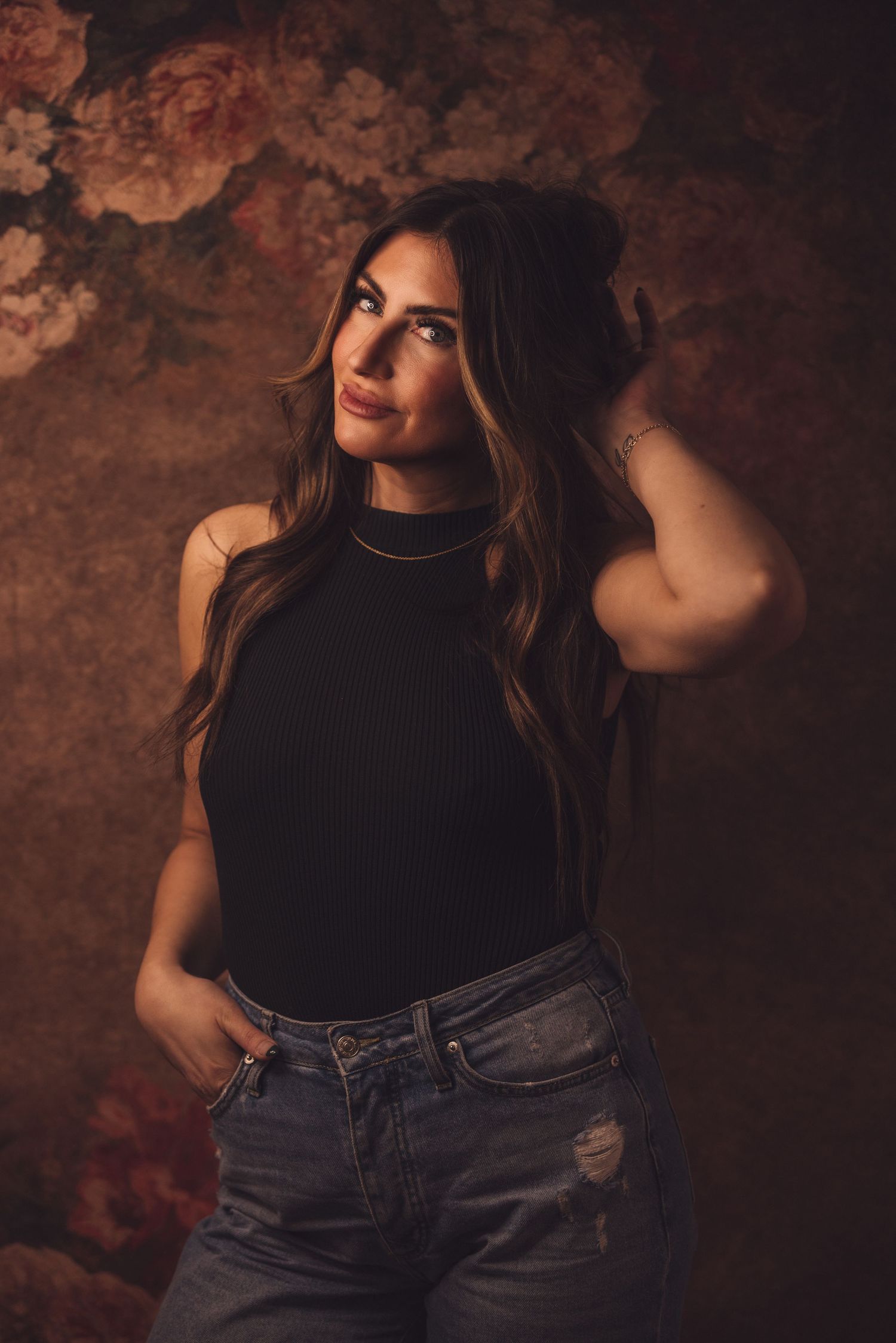 Moody portrait series against textured rust-colored backdrop wearing black top and jeans.