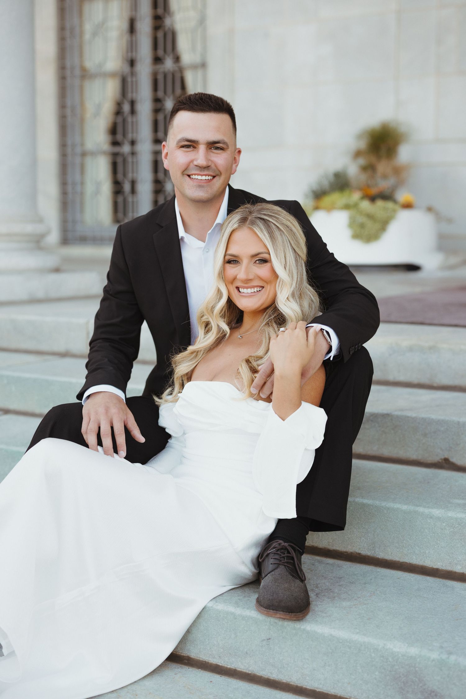 Romantic wedding couple posing on stone steps in formal attire.