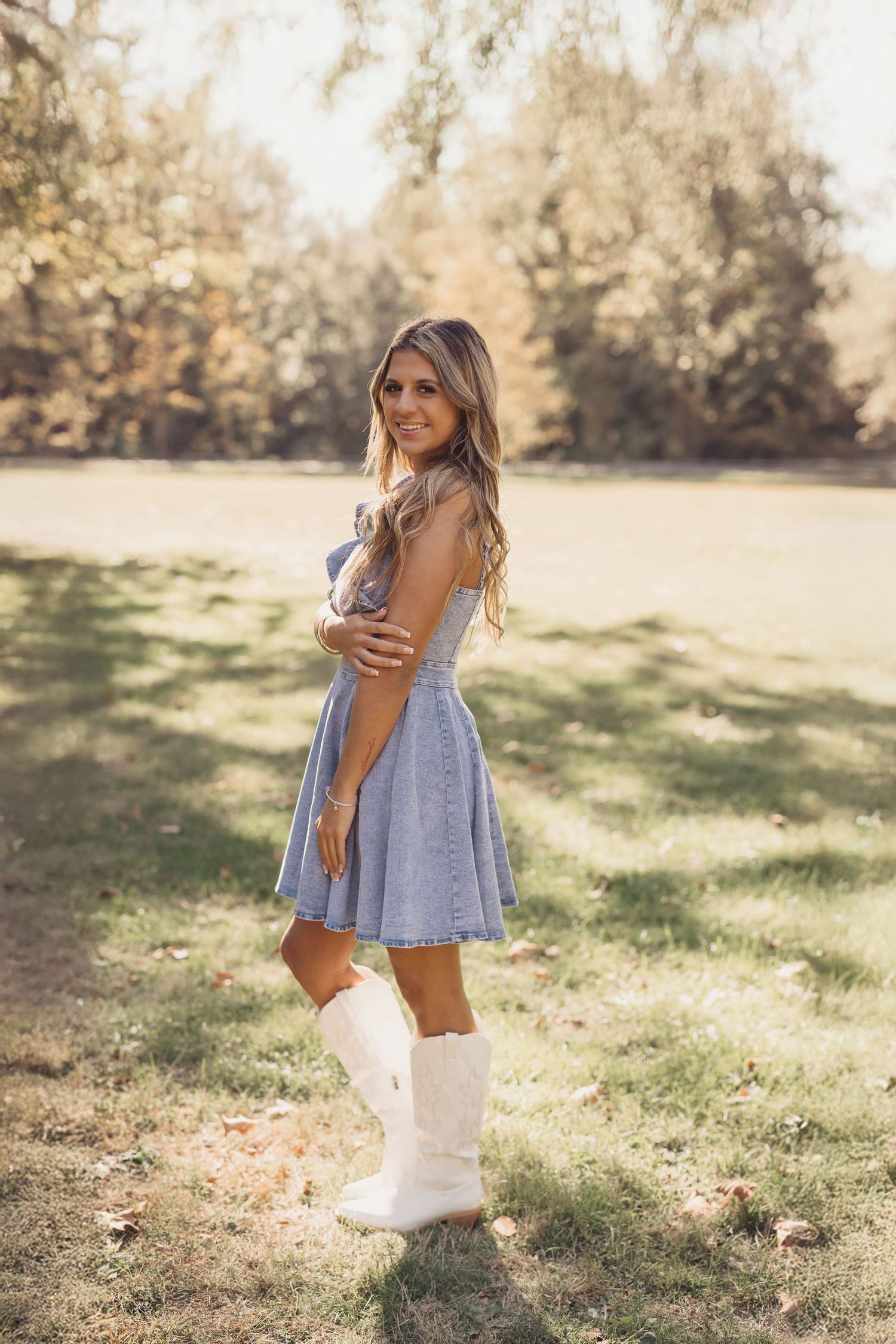 Person in blue dress and boots twirls playfully in sunlit field during autumn photoshoot.