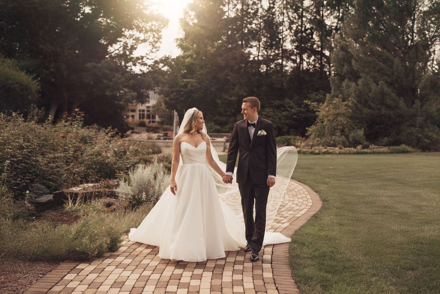 Wedding couple walking hand in hand along a brick pathway surrounded by greenery.