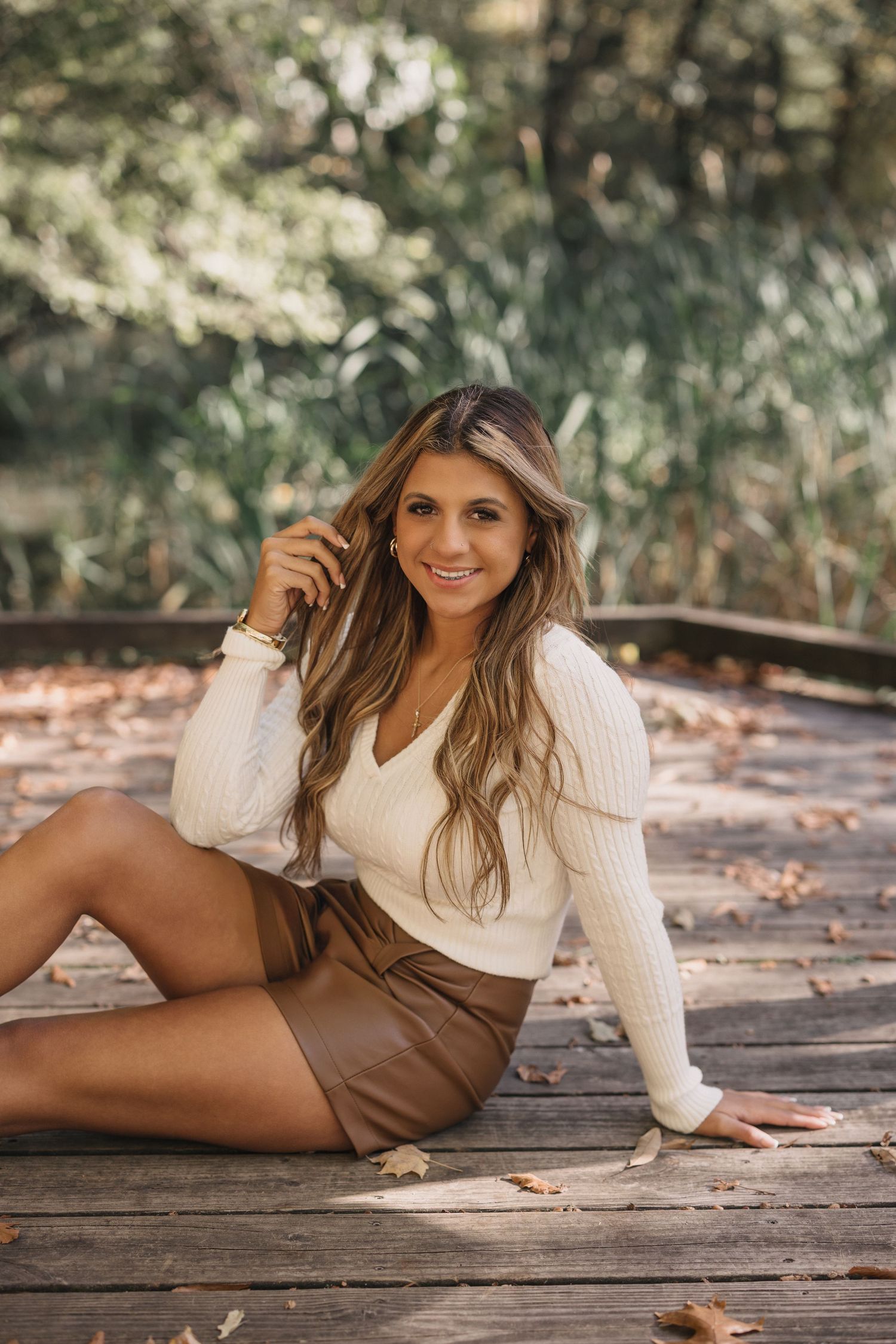 Person in cream sweater and brown shorts poses on wooden deck during outdoor photoshoot.
