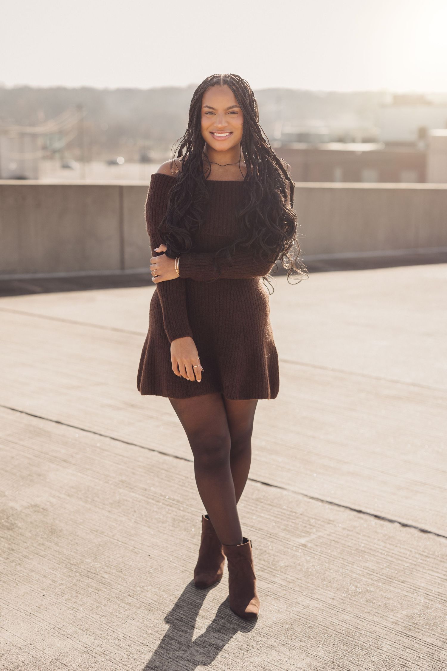Person in black outfit poses confidently on urban rooftop during sunset photoshoot.