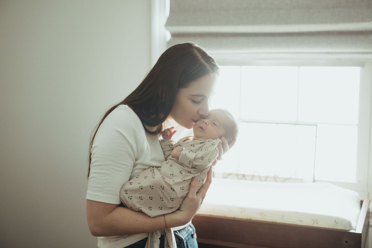 Intimate lifestyle photography session in a minimalist nursery setting with natural window light.