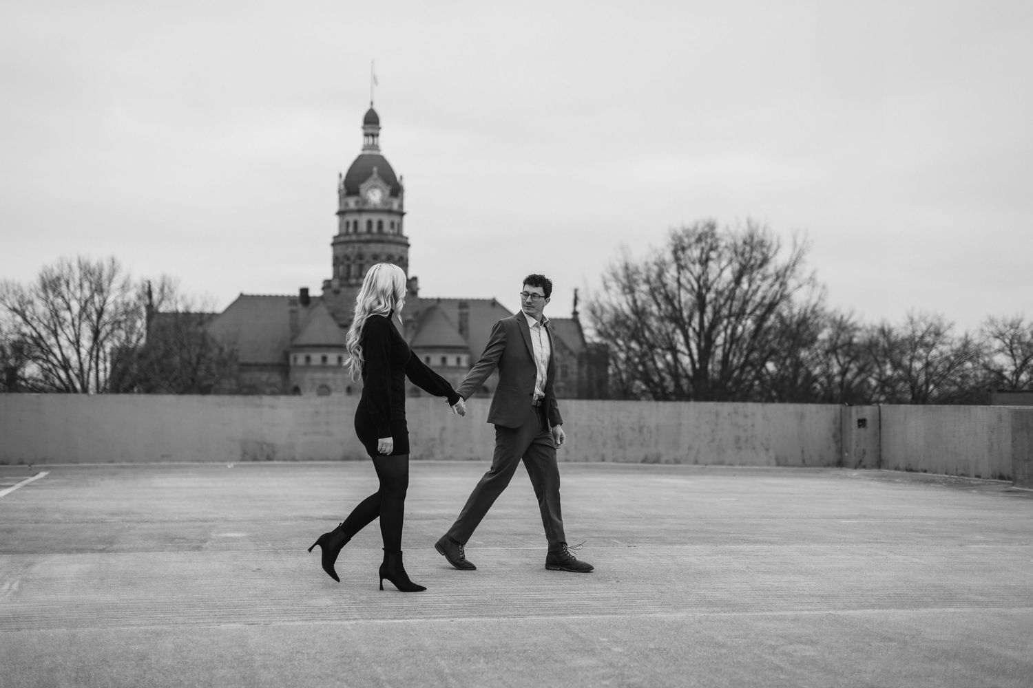 Black and white photo series of a couple walking together on a rooftop with city architecture in background.