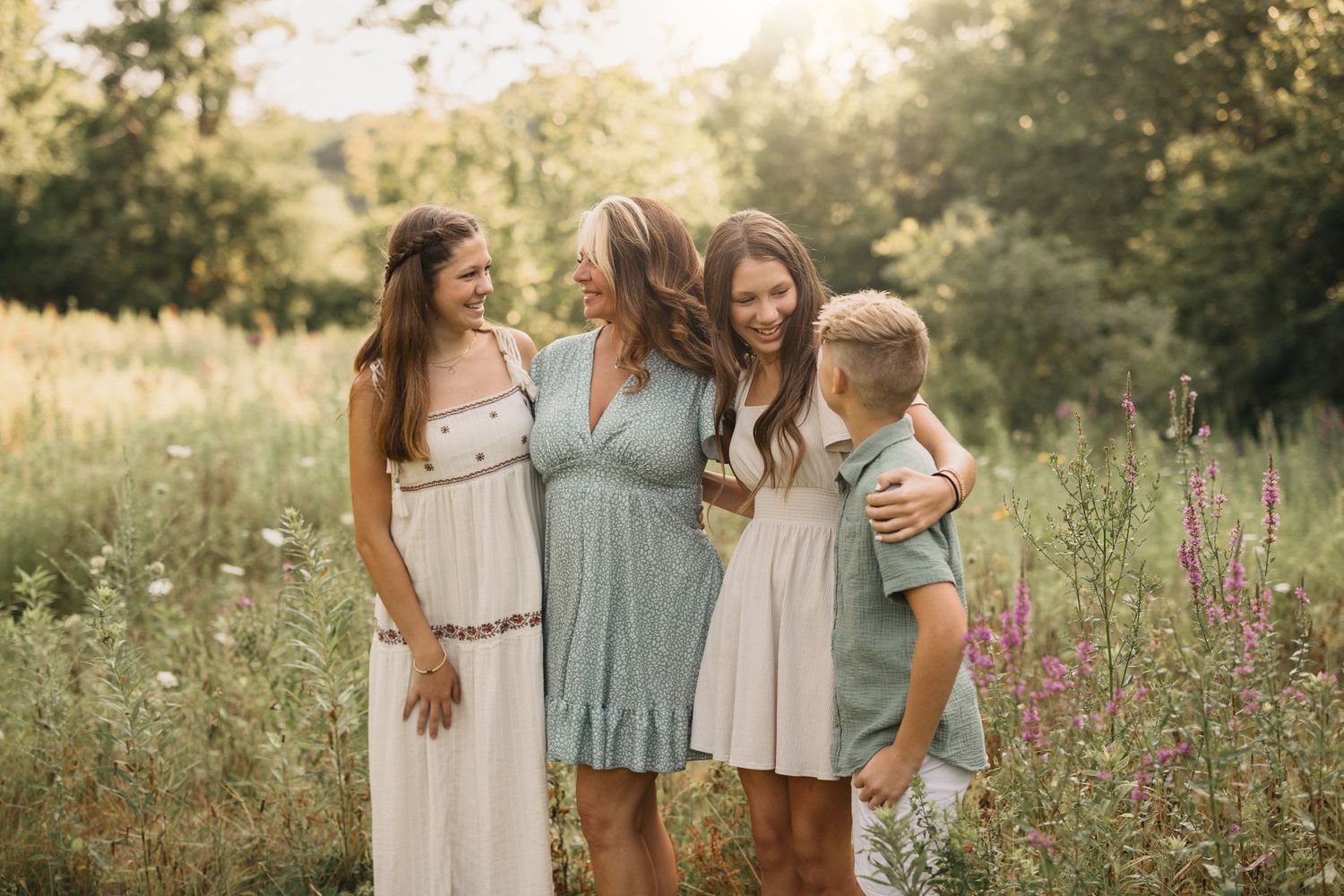 Group of friends in casual summer dresses laughing together in a sunlit meadow with wildflowers.