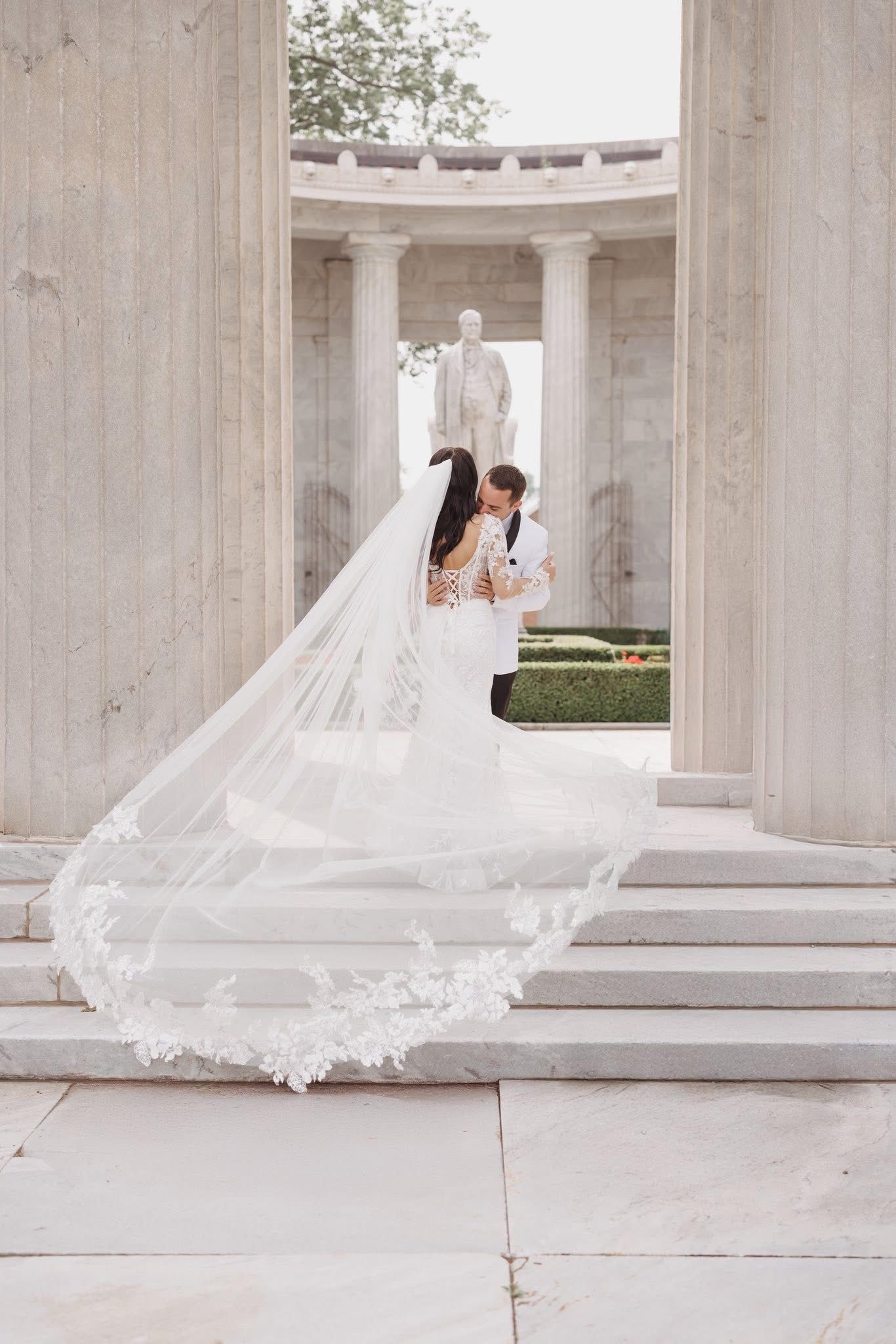 Flowing white wedding veil dramatically billowing in the wind against a white columned architectural backdrop.