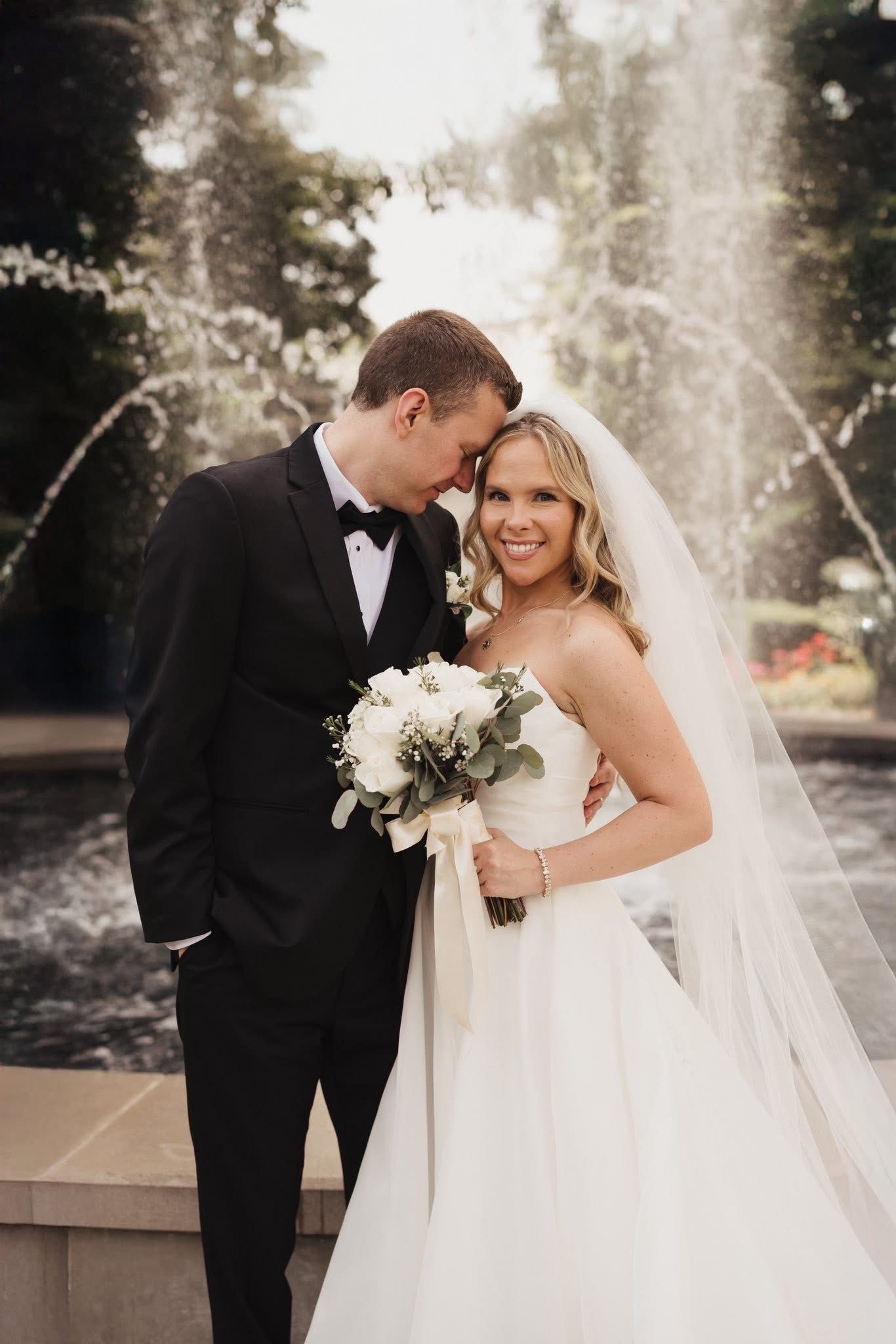 Wedding couple sharing intimate moments in formal attire against a fountain backdrop.
