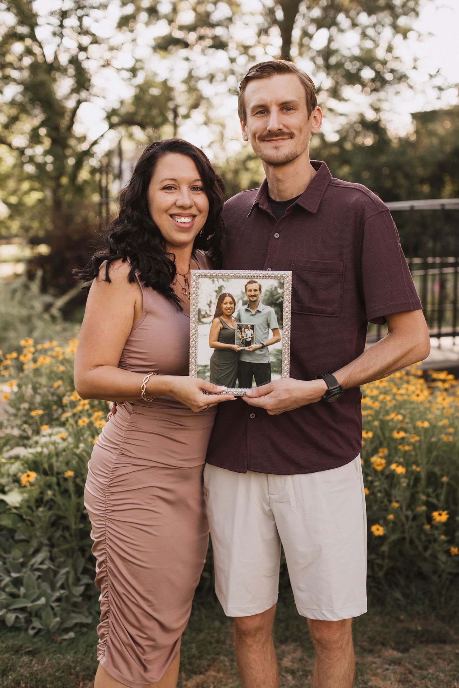 Couple holding vintage photographs in garden setting with yellow flowers blooming.