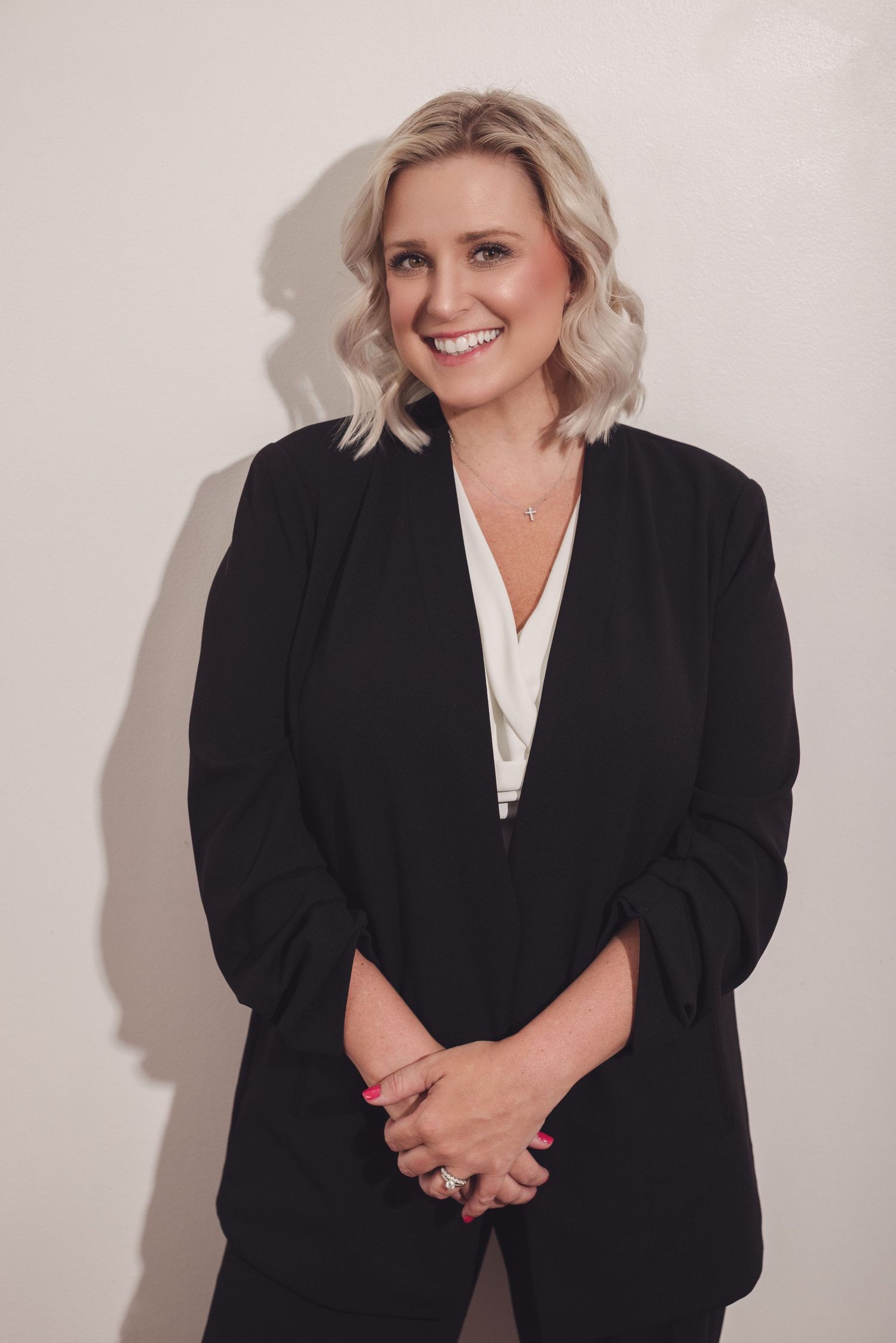 Professional studio portraits in black blazer against white backdrop.