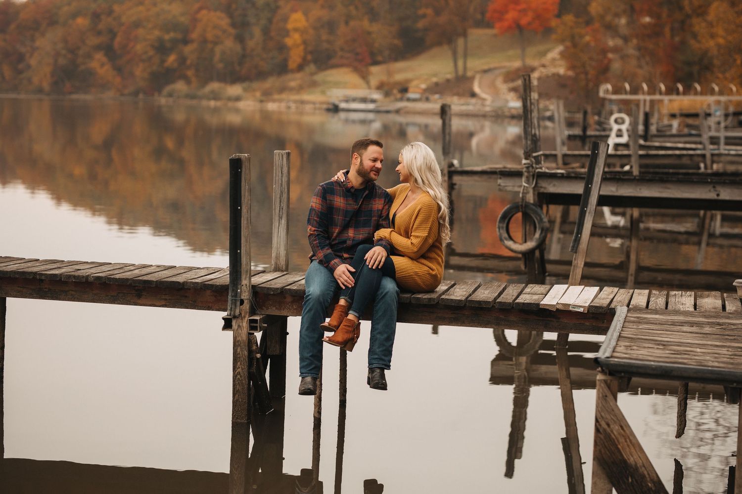 Couple sitting together on wooden dock during autumn sunset by lake.
