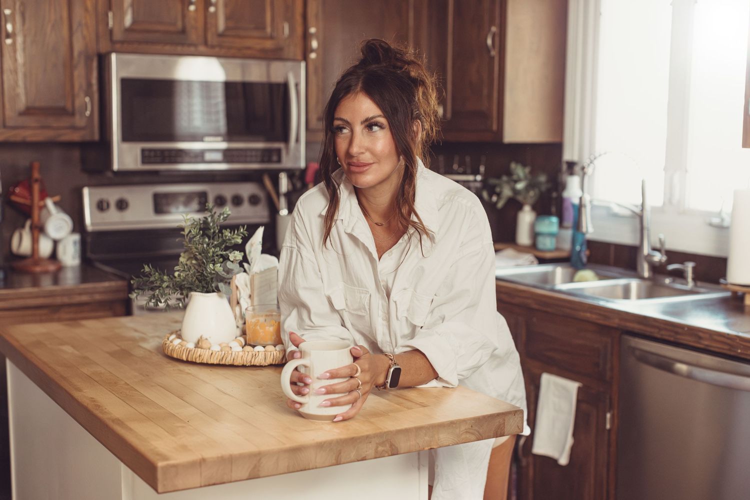 Person enjoying morning coffee while leaning on wooden kitchen counter.