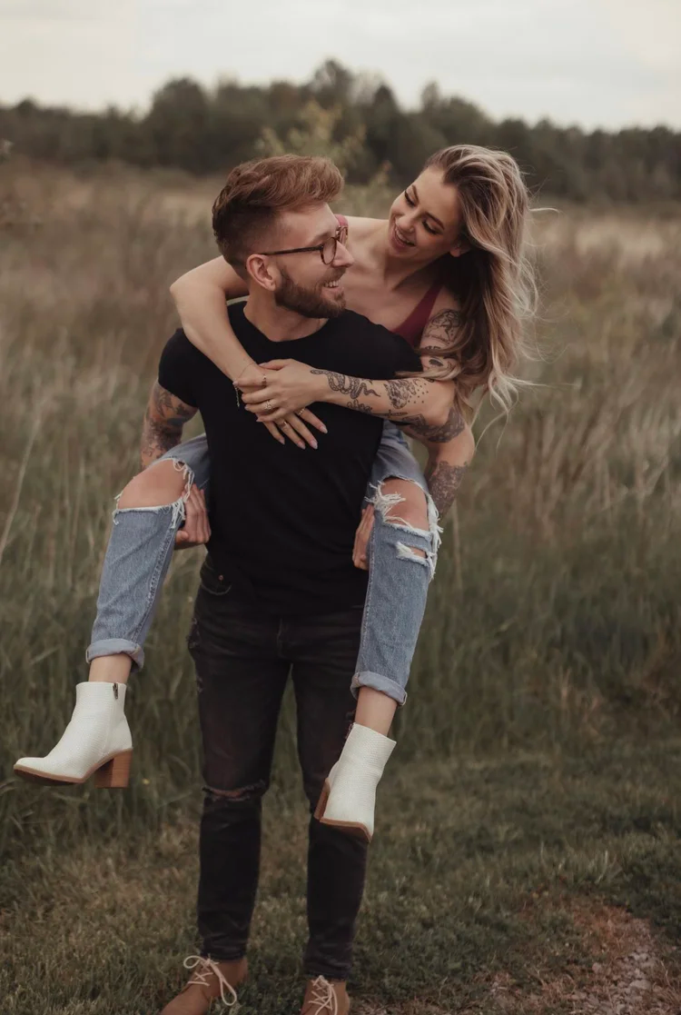 Playful couples photoshoot in a field showing piggyback rides and natural candid moments.