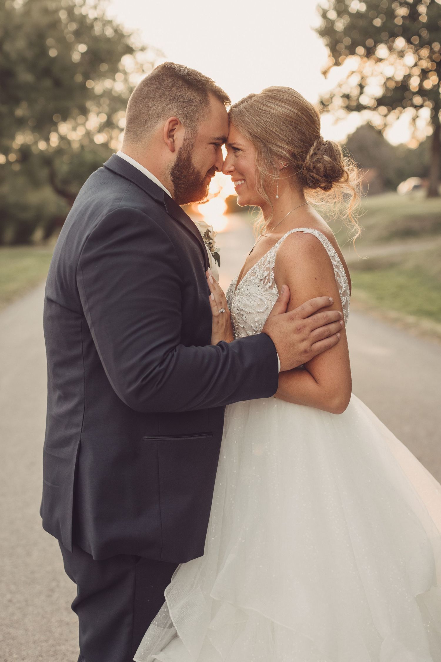 Romantic sunset wedding photos of a couple in formal attire sharing intimate moments on a country road.