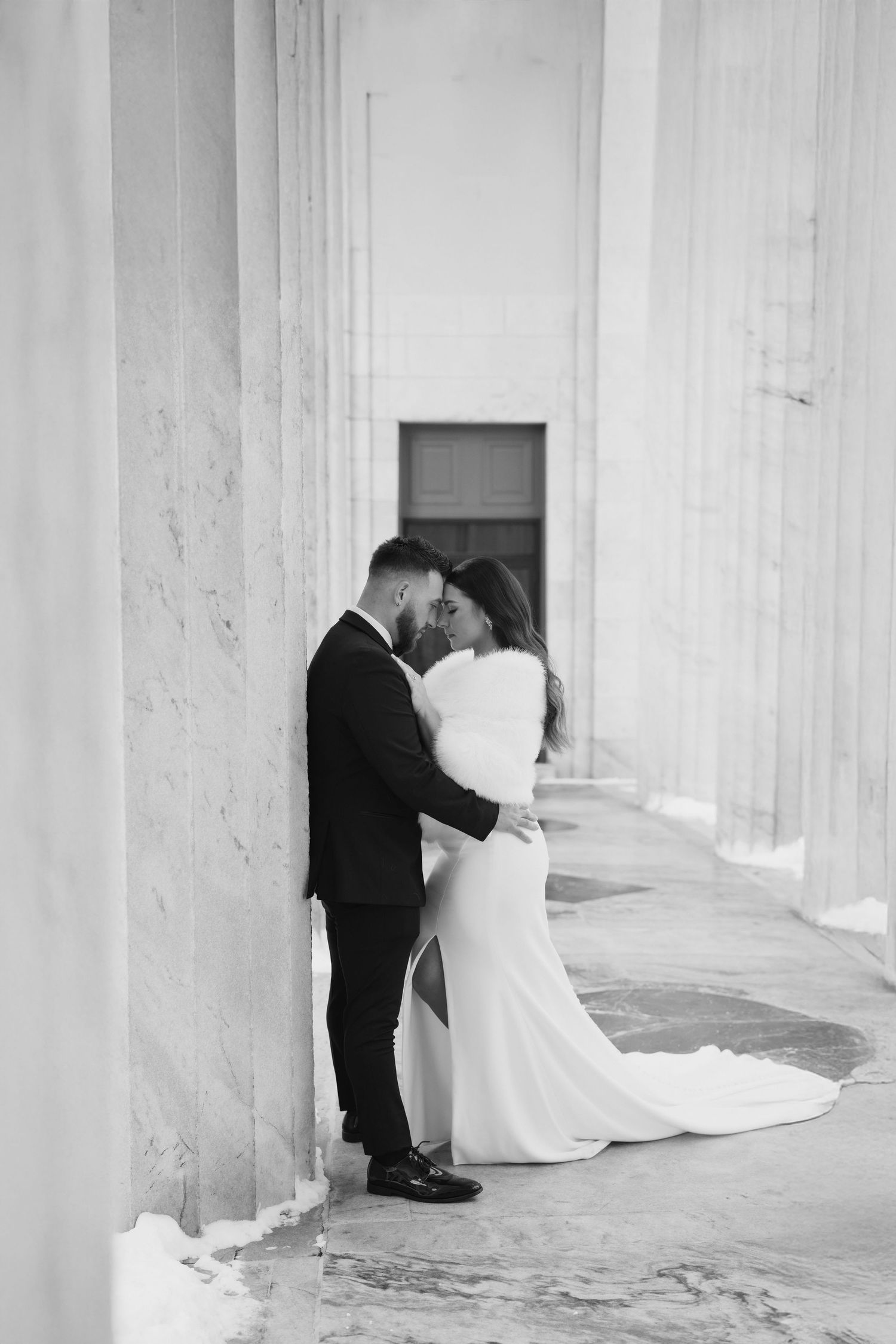 A romantic black and white wedding photo series showing intimate moments between newlyweds in a columned corridor.