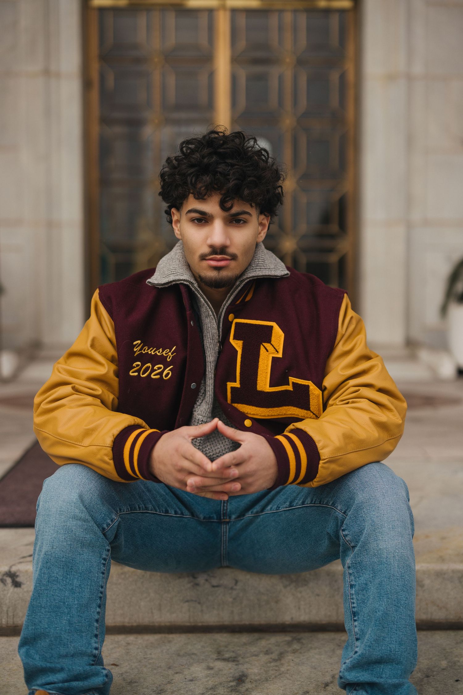 Casual portrait series of person in varsity jacket sitting on concrete steps.