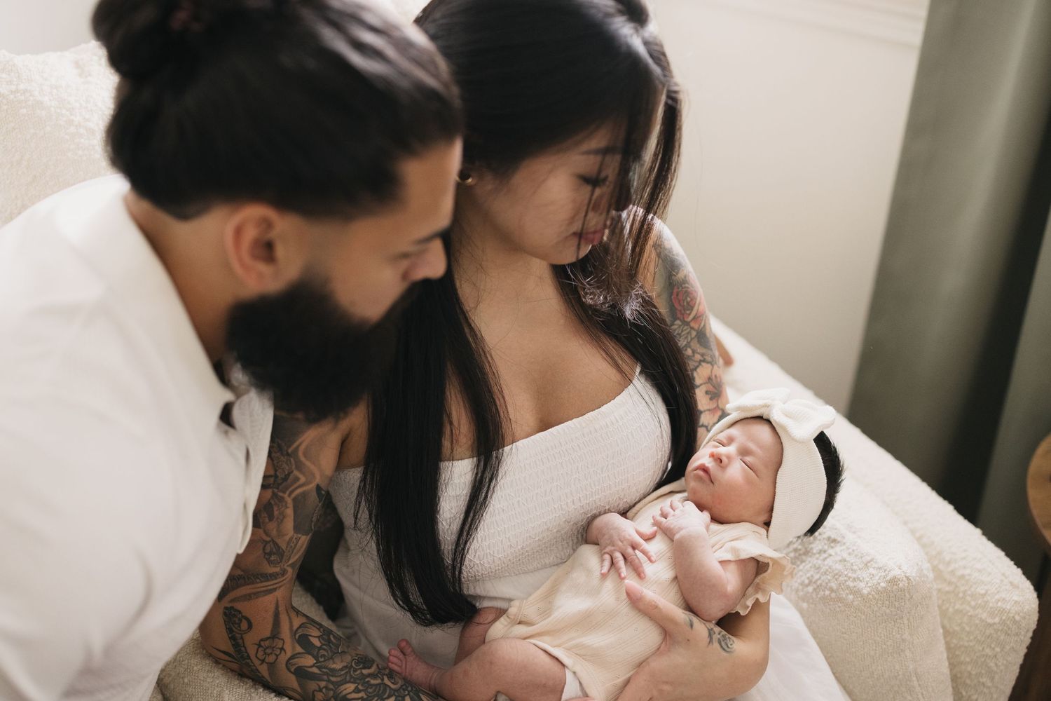 A couple sharing an intimate moment with their newborn baby on a white couch.