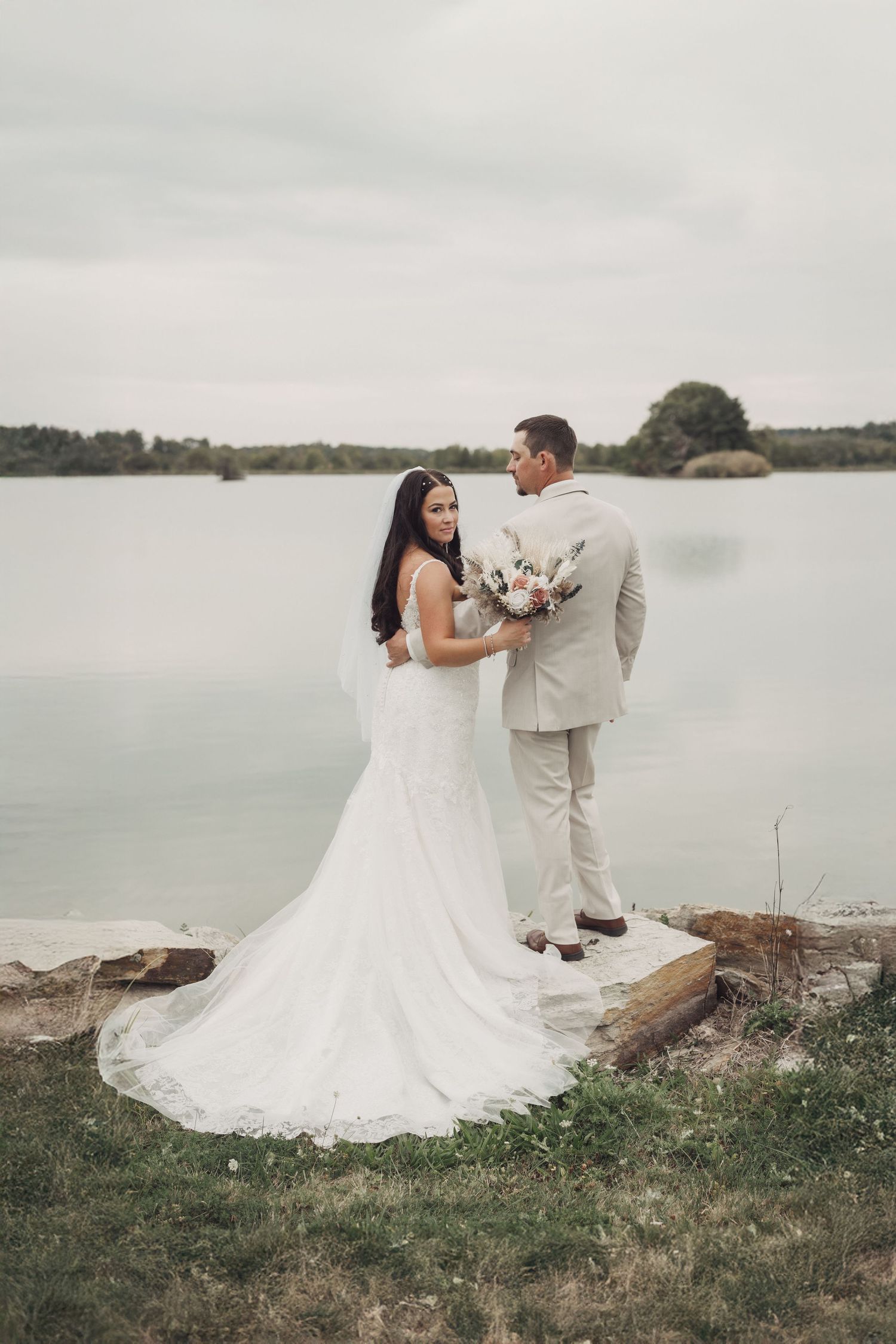 Wedding couple posing by lakeside in elegant attire.
