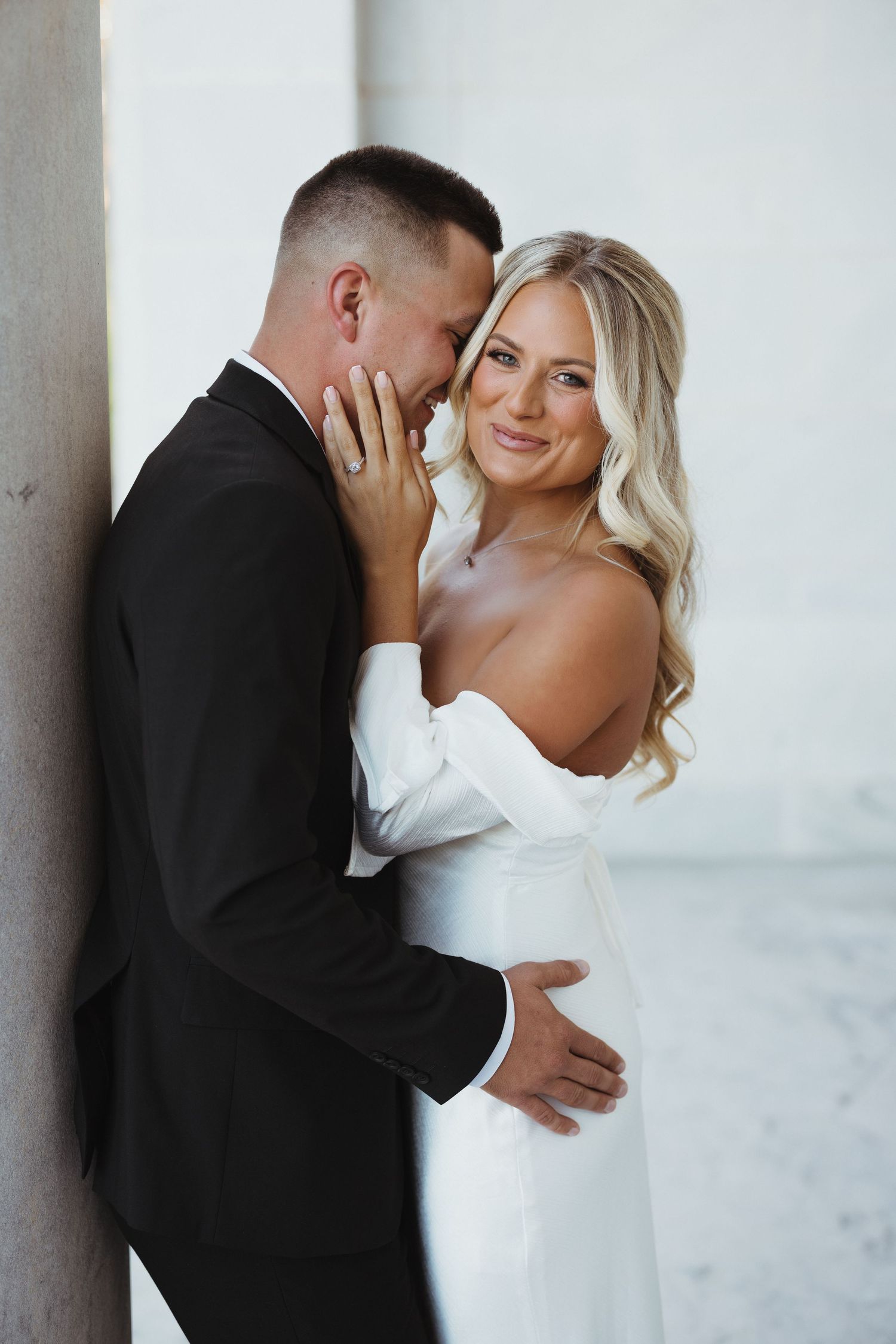 Bride in white dress and groom in black suit pose on concrete staircase during wedding photoshoot.