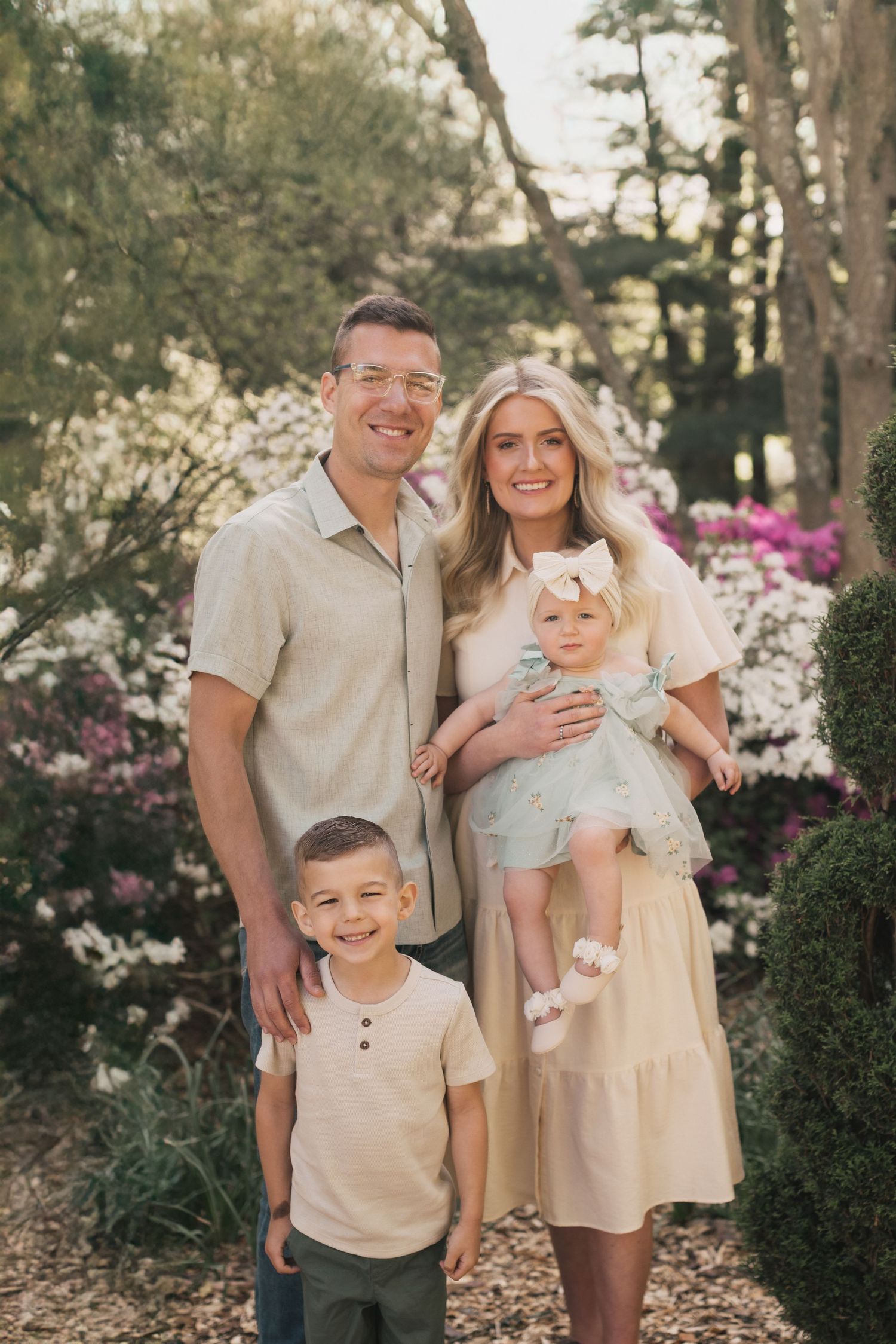 A family in coordinating neutral outfits poses together in a garden with blooming spring flowers.