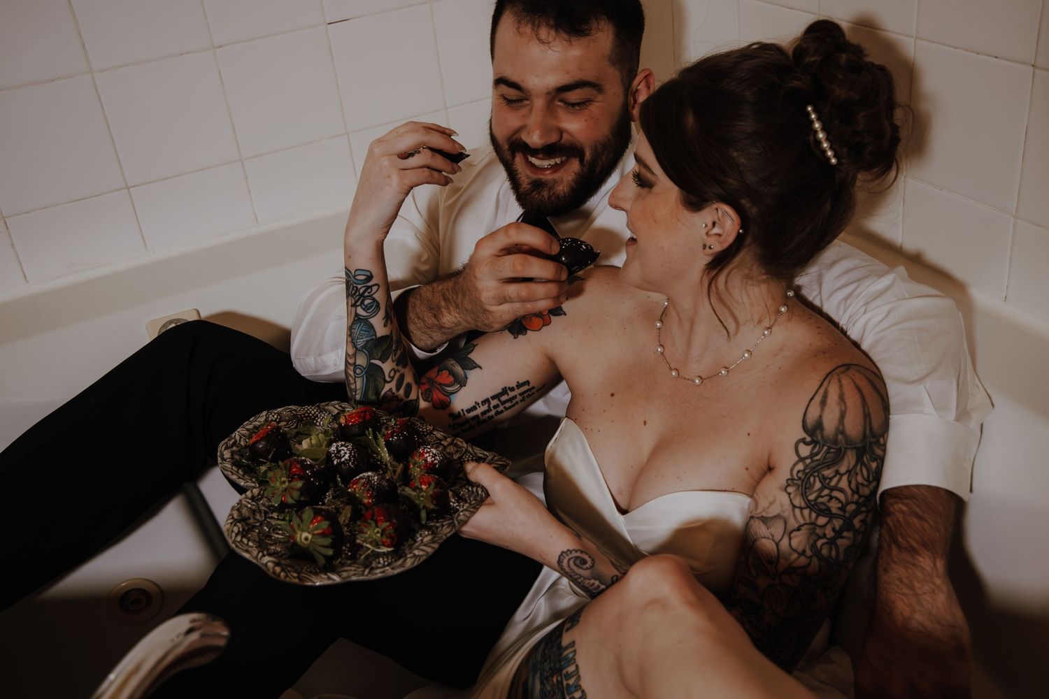 A couple shares a romantic moment while eating a salad together in casual wedding attire.