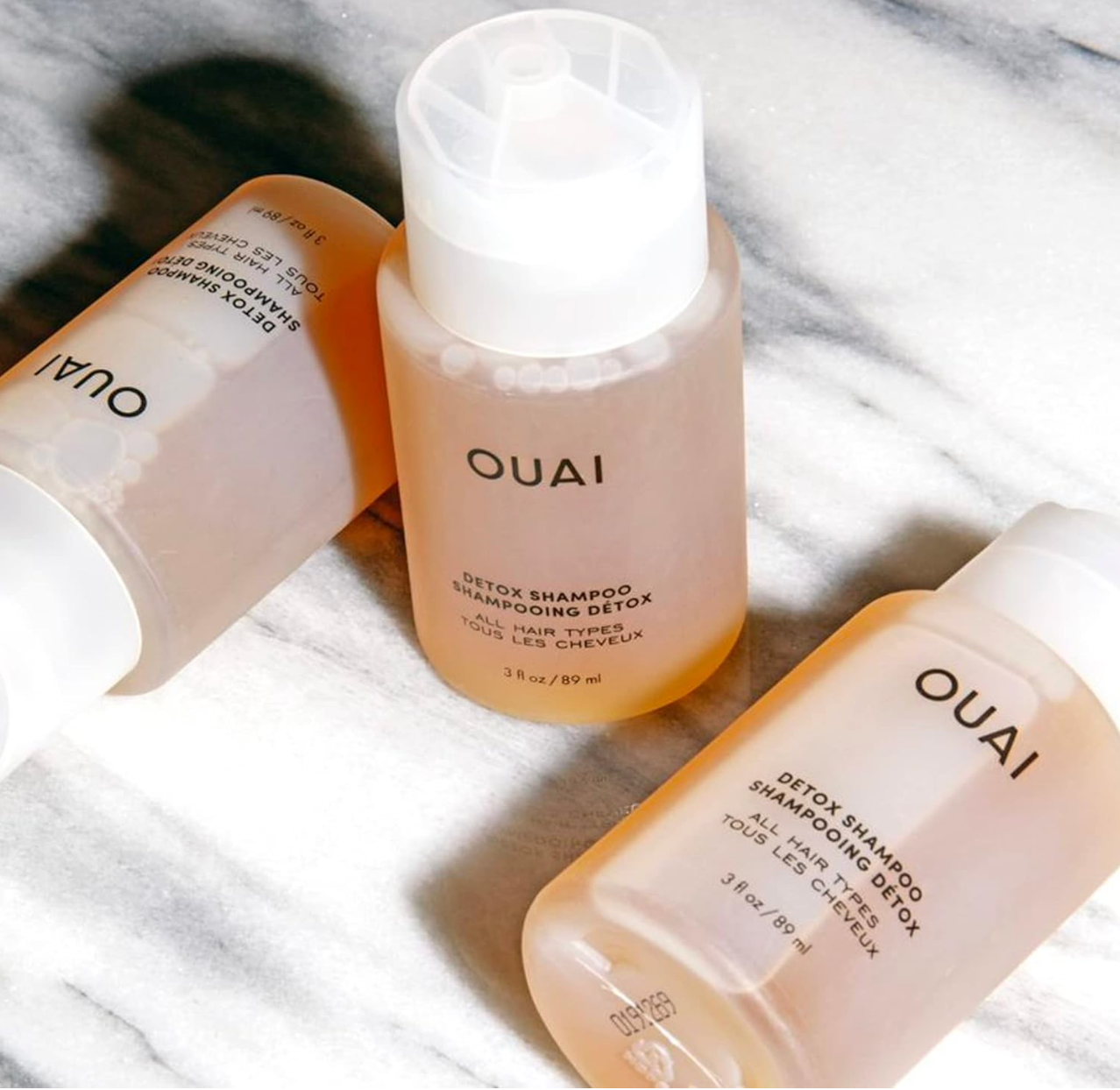 Three Ouai hair care products with transparent bottles on marble surface.