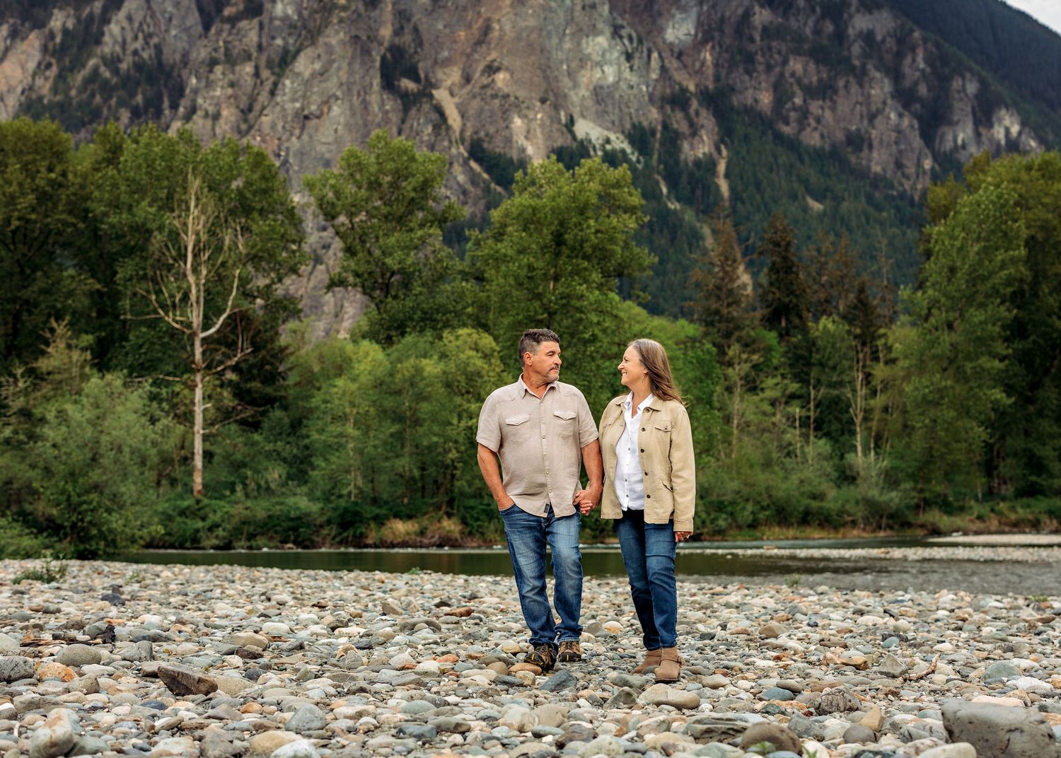 Scenic mountain engagement photo session on rocky riverbank with dramatic cliffs in background.