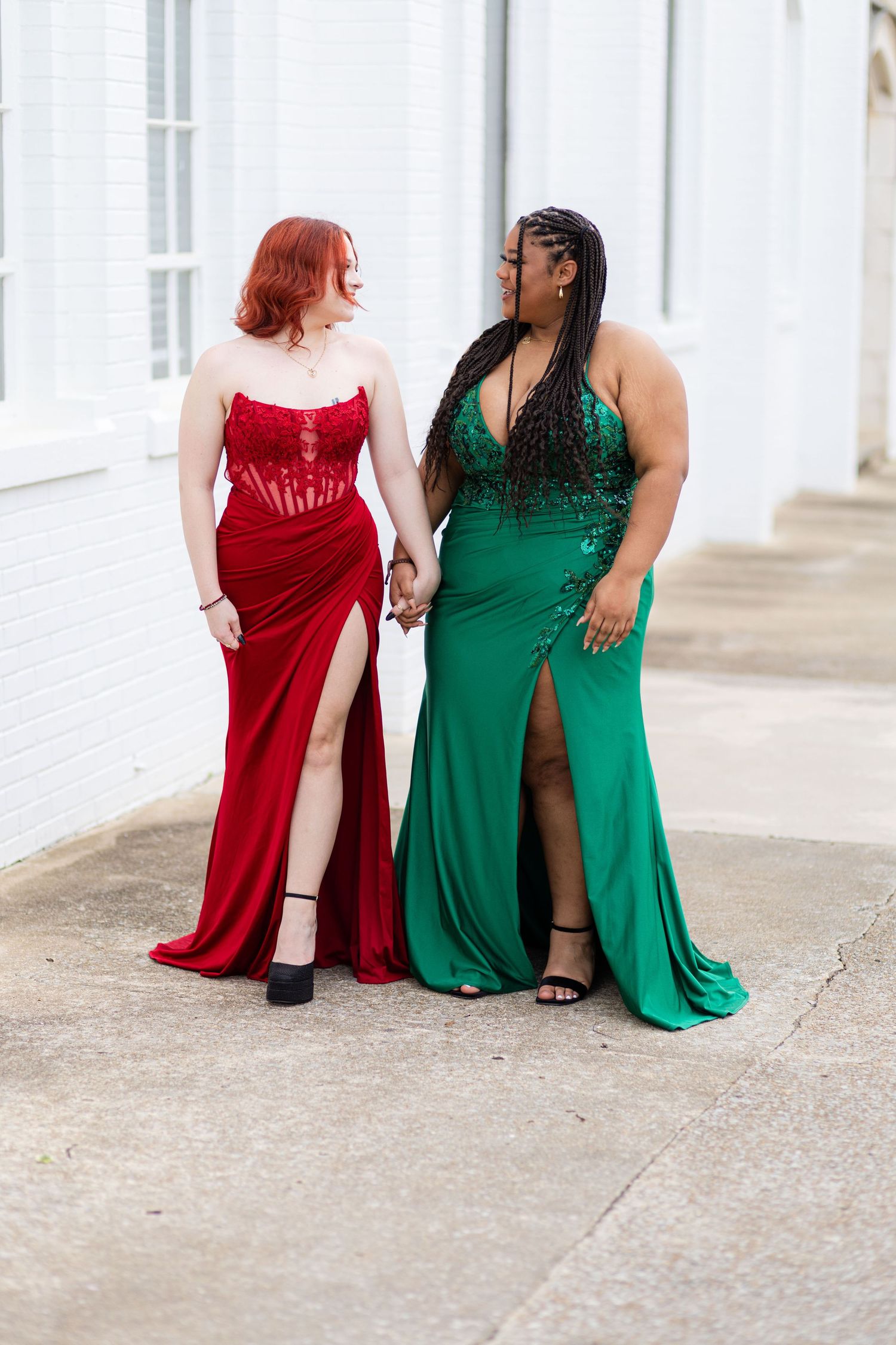 Two high school seniors in prom dresses walking down sidewalk