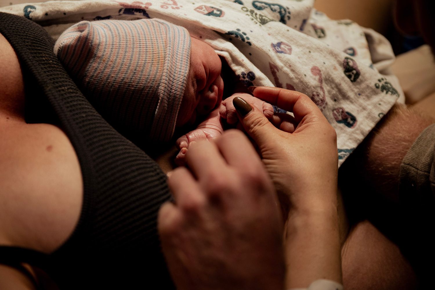 Newborn baby in striped hat resting on mother's chest during skin-to-skin contact after birth.